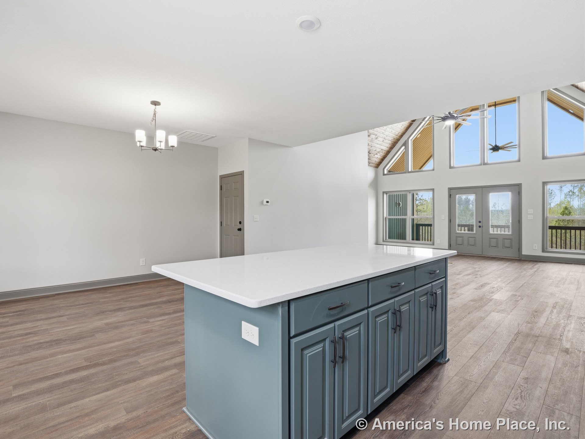 Vaulted ceiling with exposed beams, large triangular windows, double glass doors, open concept layout, blue kitchen island cabinetry with white quartz countertop, wood-look