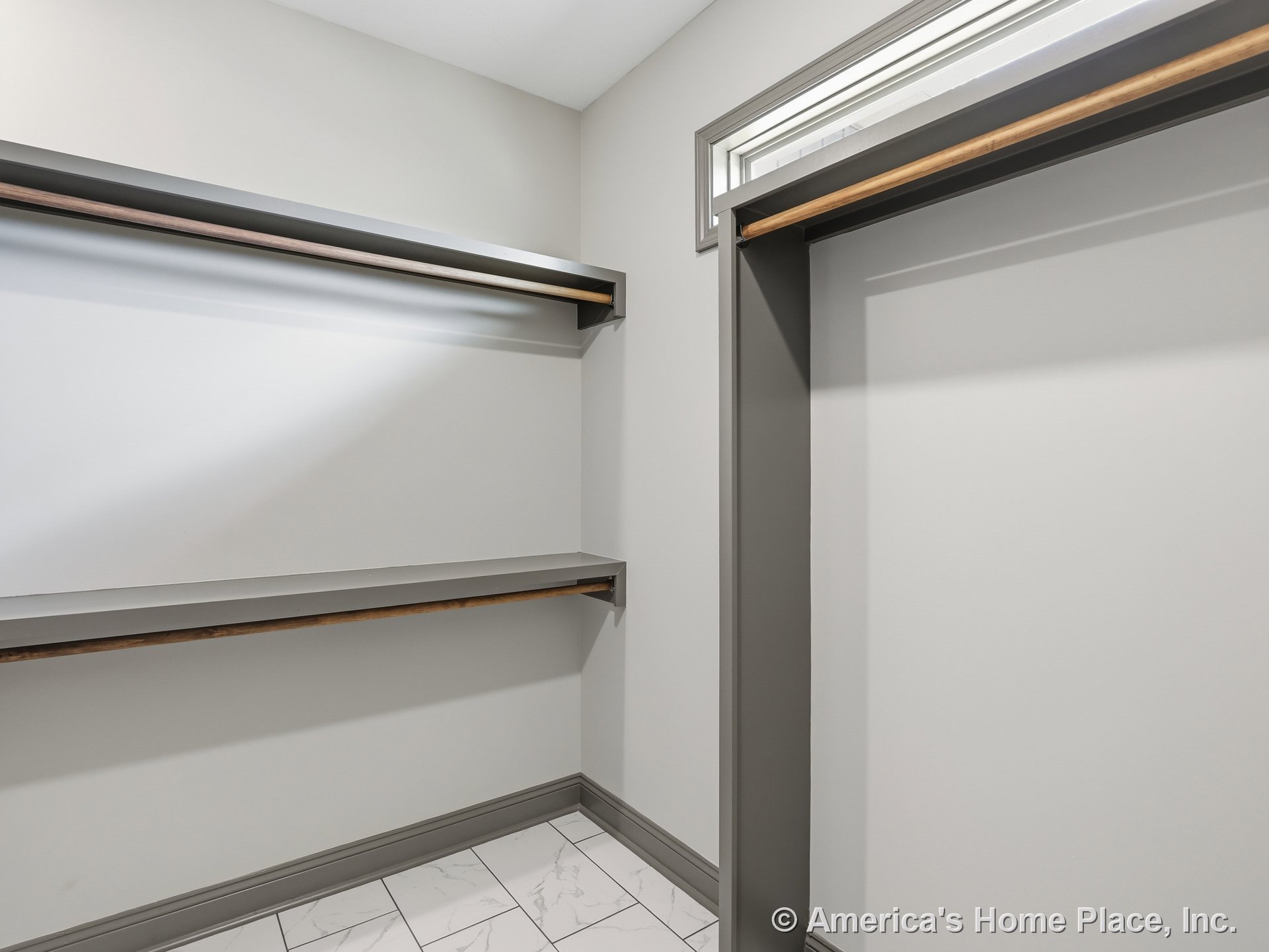Walk-in closet with built-in gray shelving and hanging rods, tile flooring, trimmed window, neutral wall color, and baseboard trim.