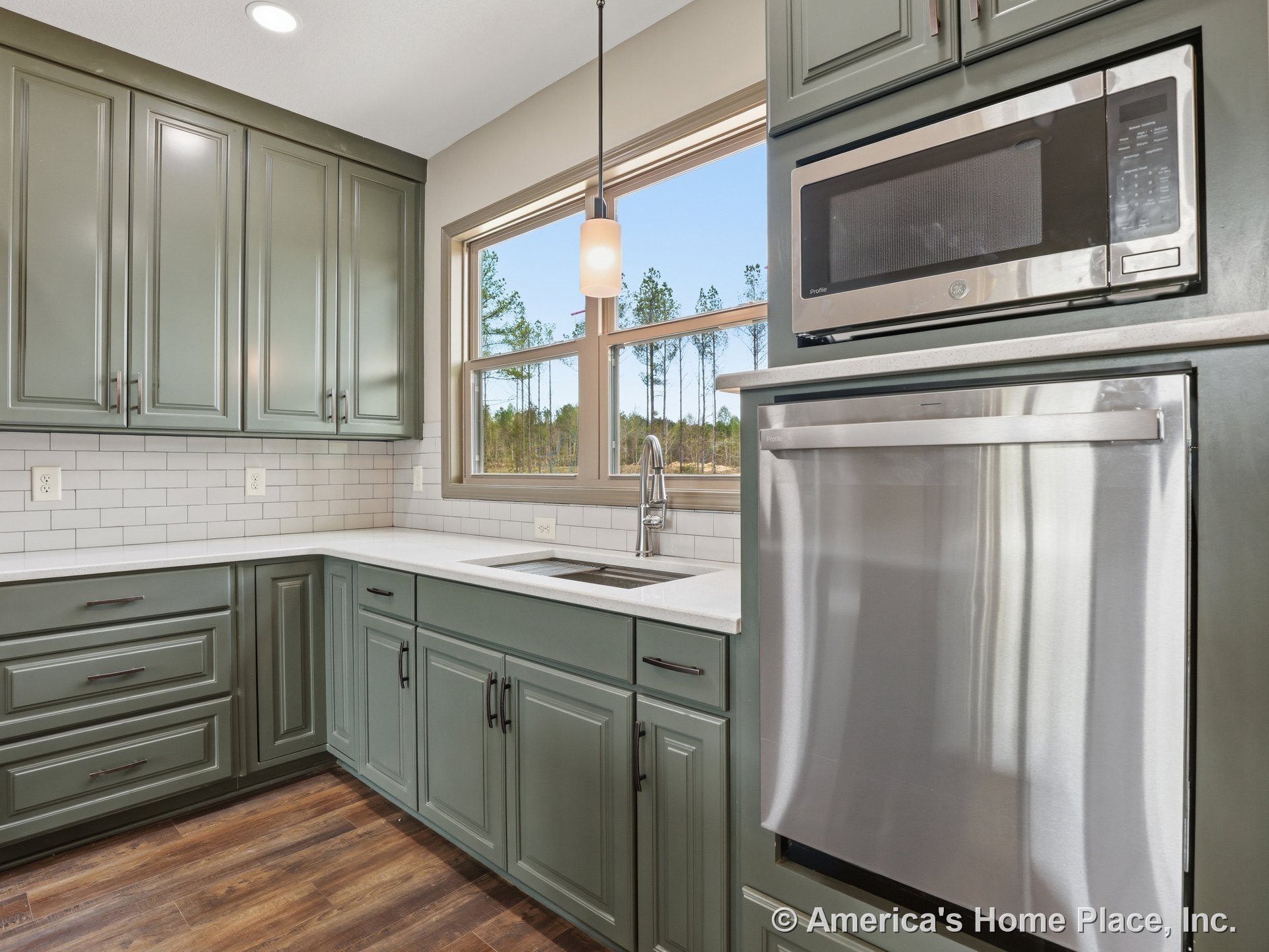 Green kitchen cabinetry with quartz countertops, subway tile backsplash, stainless steel appliances including built-in microwave and under-counter dishwasher, large window above