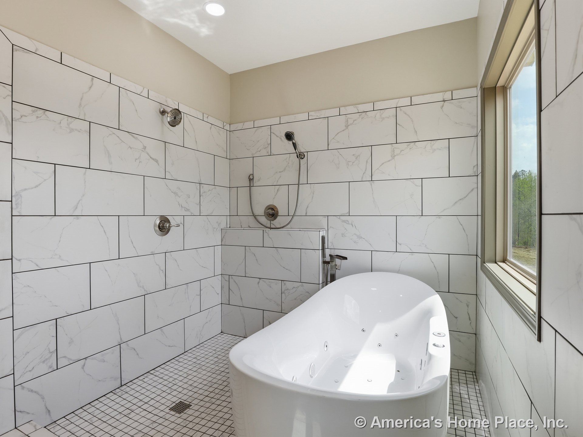 Freestanding soaking tub beside walk-in shower area, large-format marble-look tile walls, square mosaic floor tile, window with trim, recessed ceiling light, modern built-in