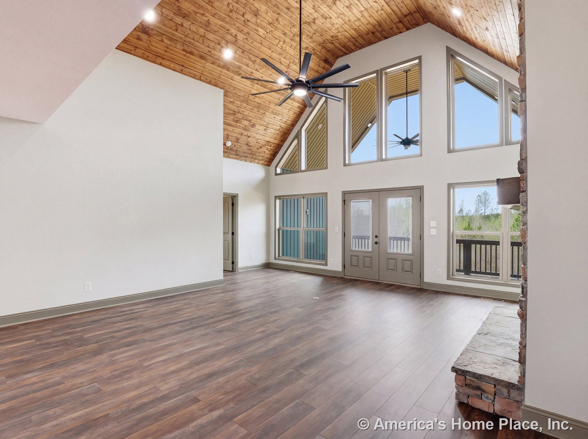 Vaulted wood ceiling with recessed lighting, expansive triangular windows and double glass doors, stone fireplace hearth, wood-look flooring, and crisp trim detailing.