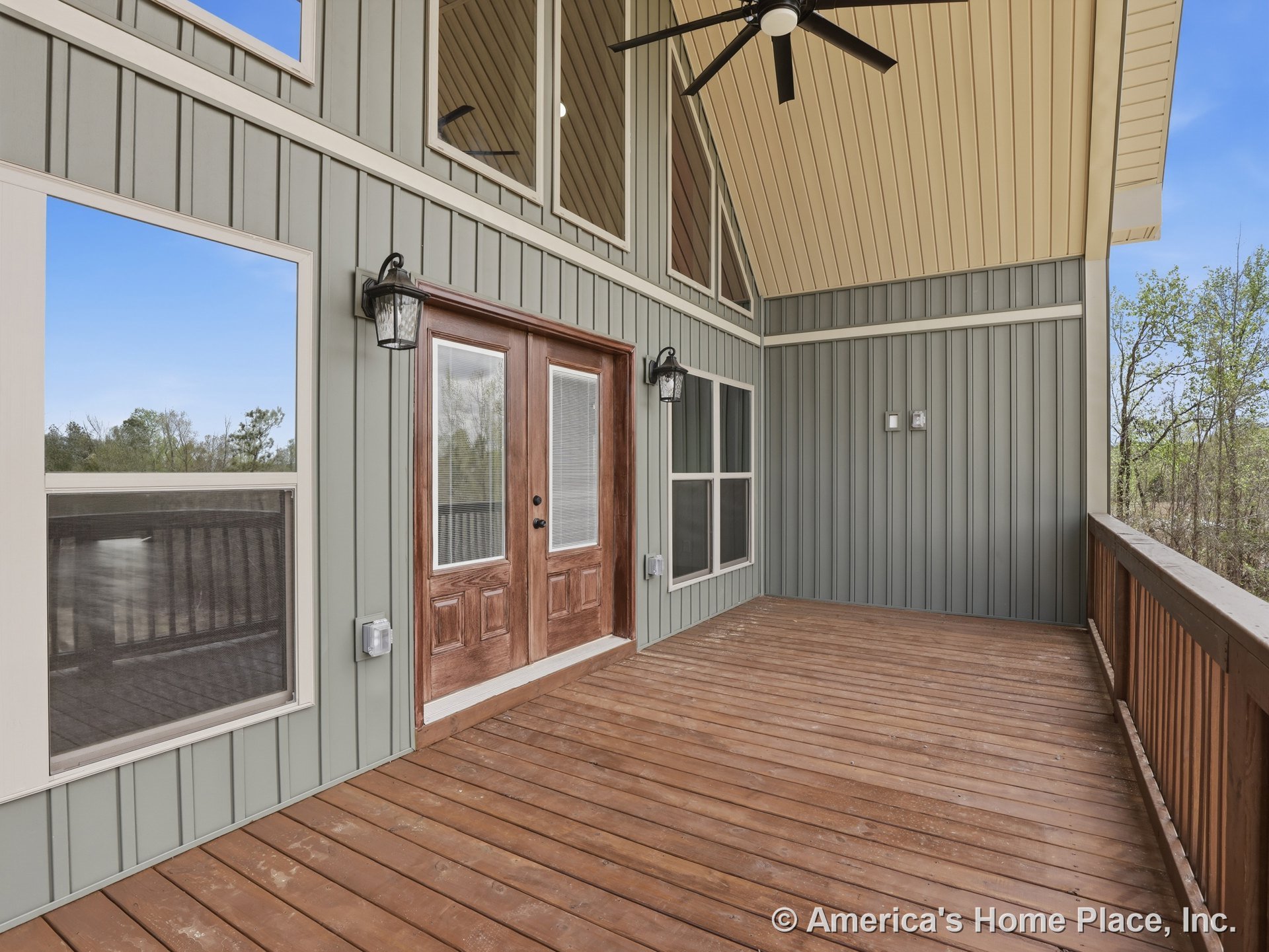 Covered porch with wood plank flooring, vertical panel siding, double glass doors, large windows, ceiling fan, wall-mounted lantern lights, exterior trim, railing, and high