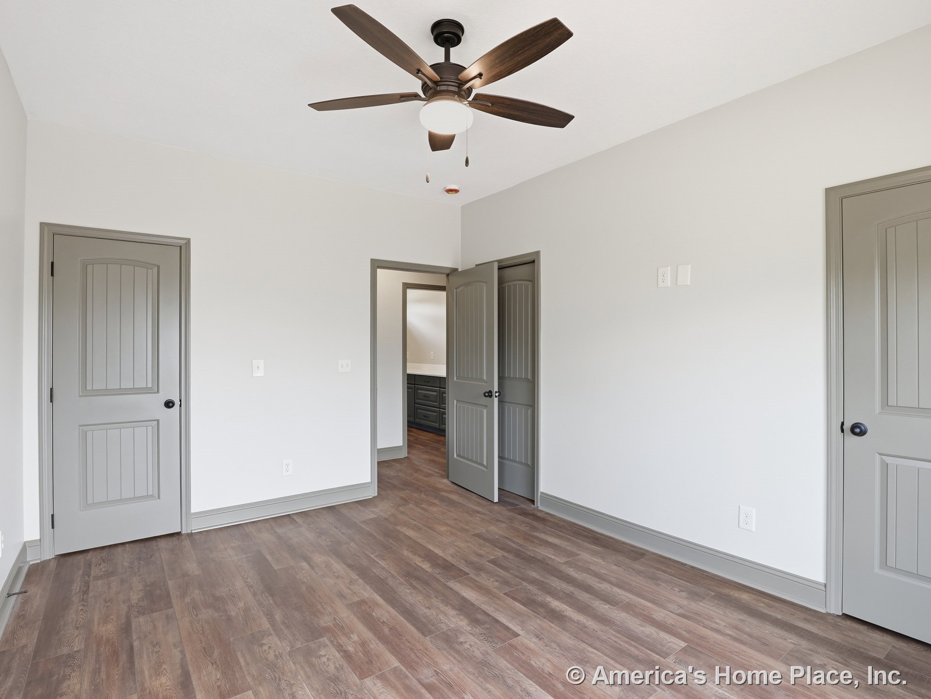 Bedroom with wood-look flooring, gray paneled doors, gray baseboards and trim, neutral wall color, ceiling fan with light, and view of adjacent bathroom cabinetry.