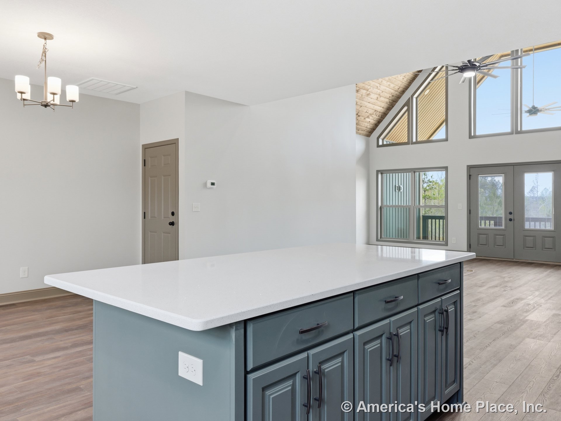Vaulted ceiling with wood accent, expansive triangular window wall, gray kitchen island cabinetry topped with white quartz countertop, modern chandelier lighting, double entry