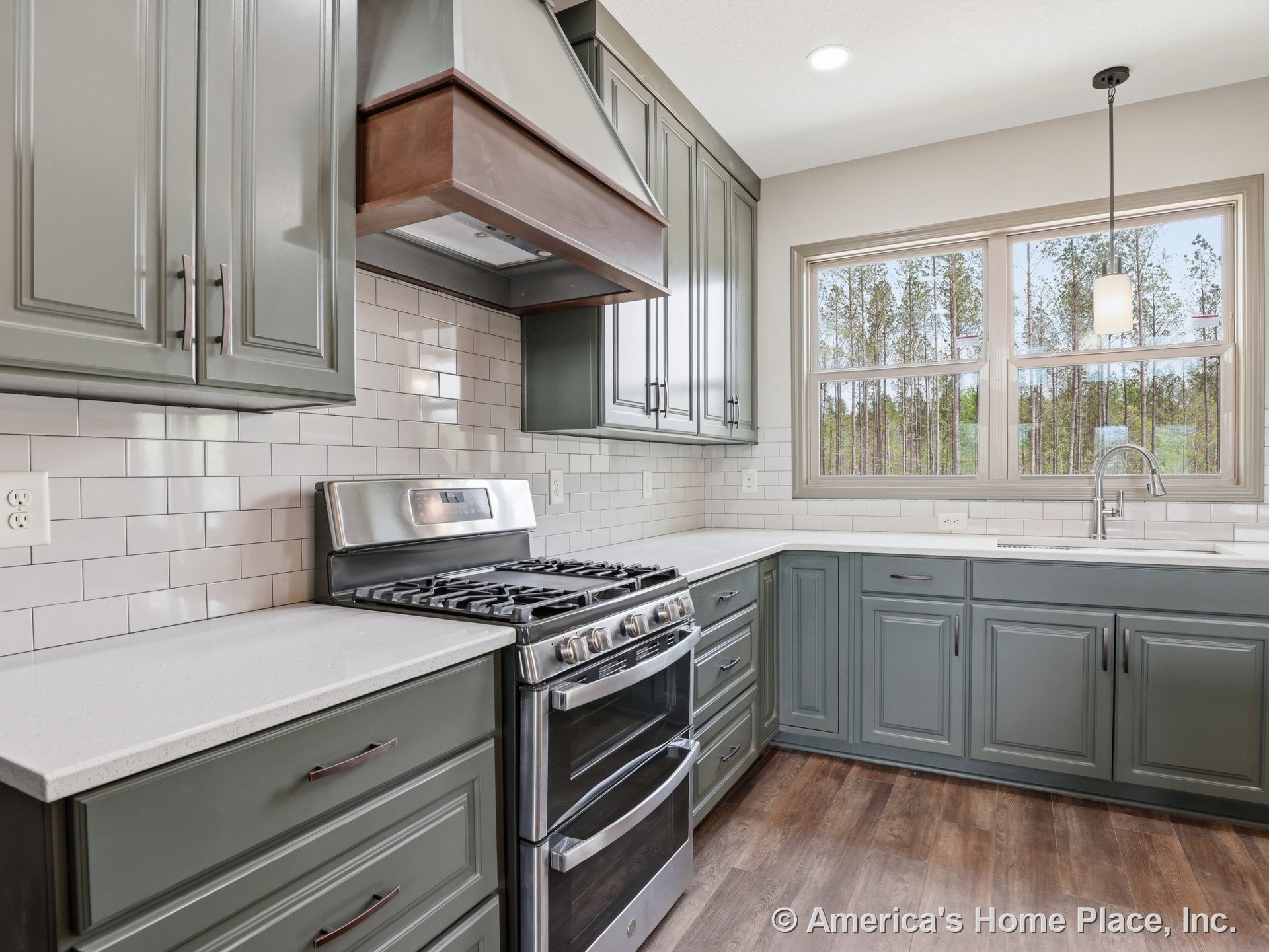 Green cabinetry kitchen with quartz countertops, subway tile backsplash, stainless steel gas range and built-in range hood, large double window above undermount sink, pendant light