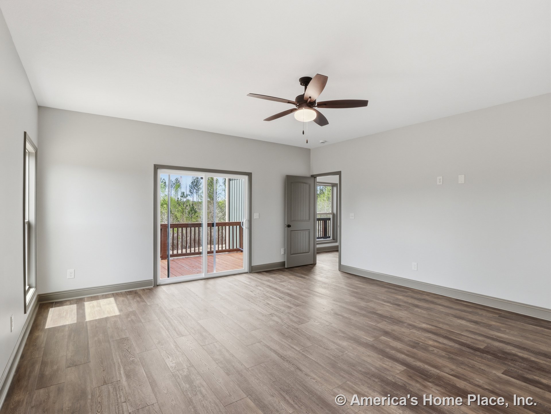 Spacious interior room with wood-look plank flooring, ceiling fan with integrated light, sliding glass doors leading to a covered porch with railing, gray trim and doors, and large
