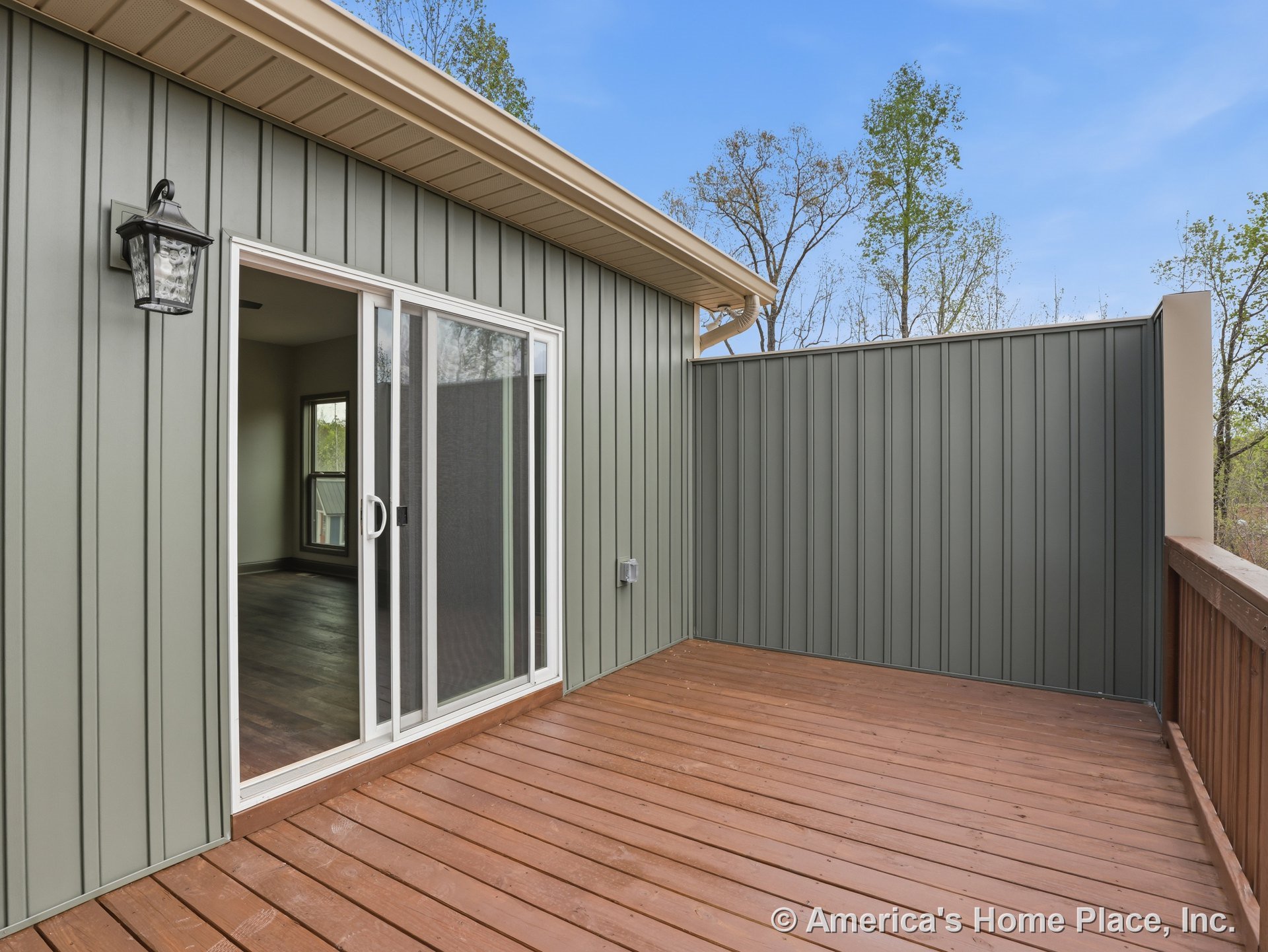 Wood deck with horizontal planks, vertical metal siding, sliding glass door, outdoor wall lantern, privacy wall, and exterior trim.