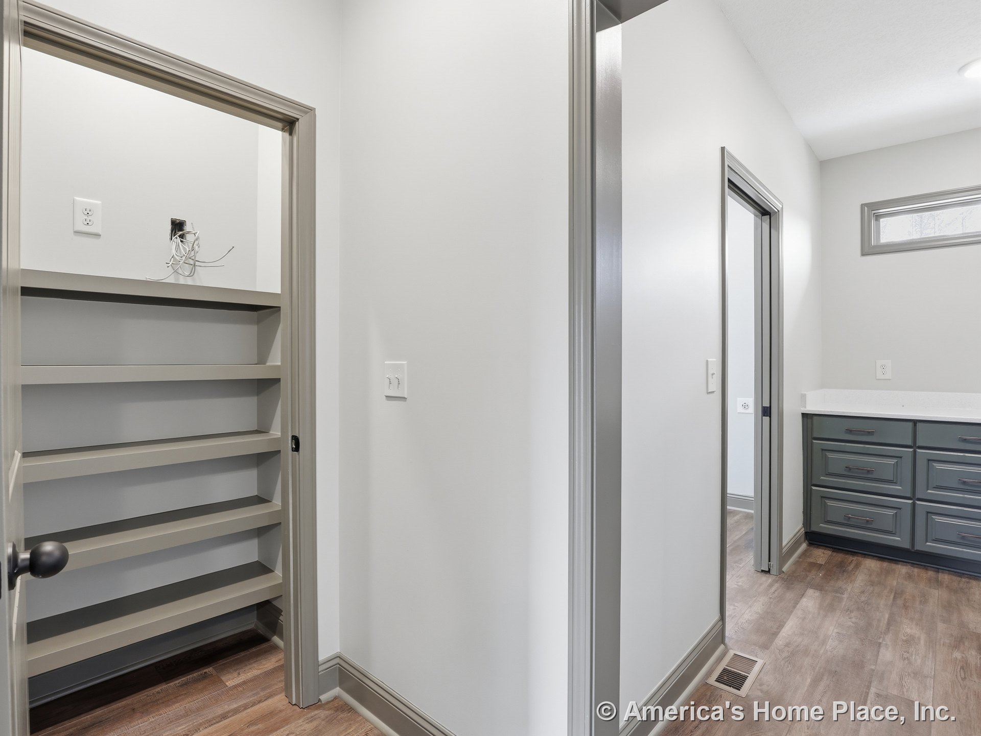 Hallway with built-in shelving, gray trim, wood-look vinyl flooring, quartz countertop atop drawer cabinetry, recessed lighting, window, baseboards, and modern door hardware.