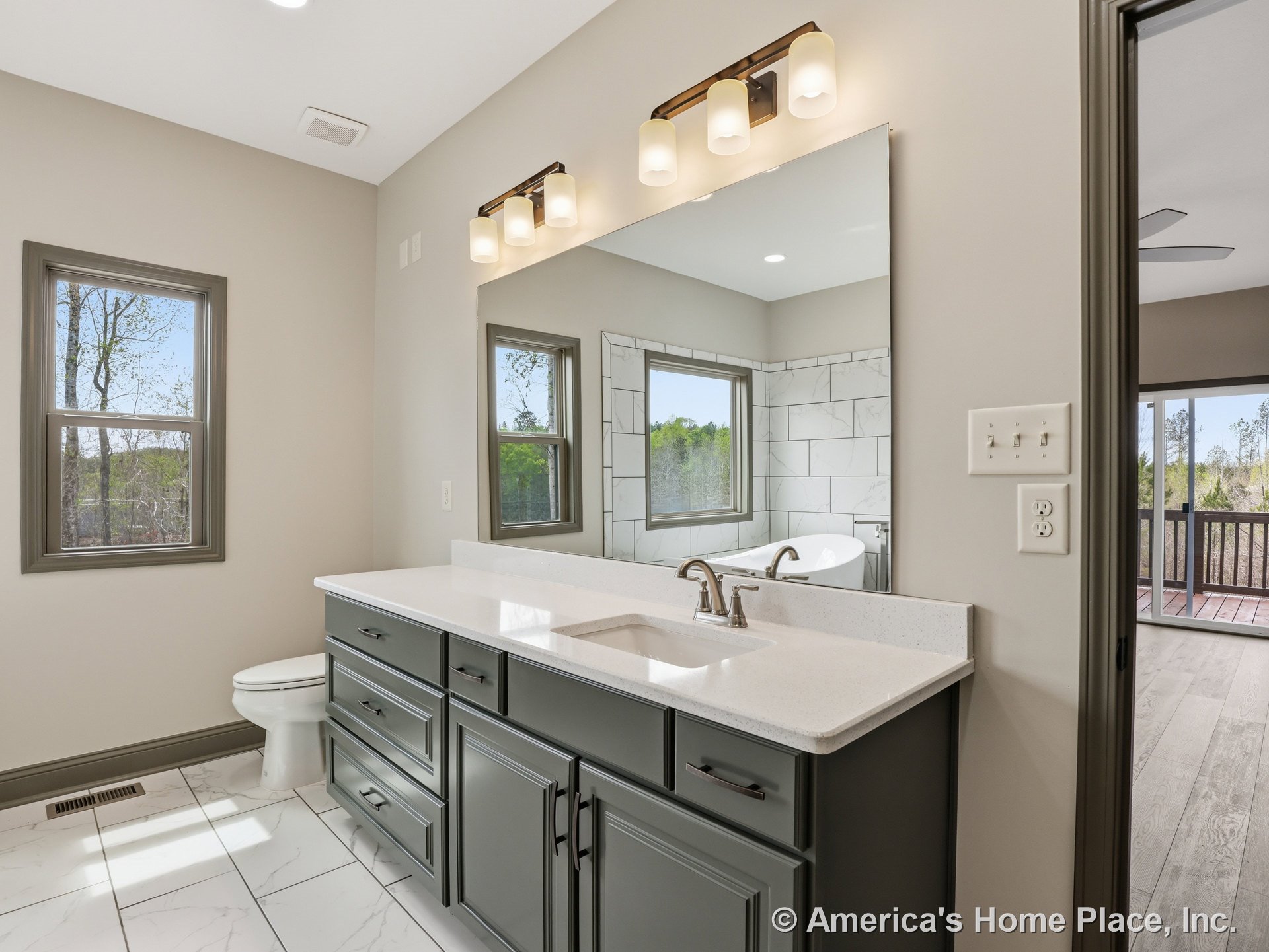 Double-sink vanity with quartz countertops and shaker-style built-in cabinetry, large wall mirror, three-light vanity fixture, gray framed windows, marble-look tile flooring