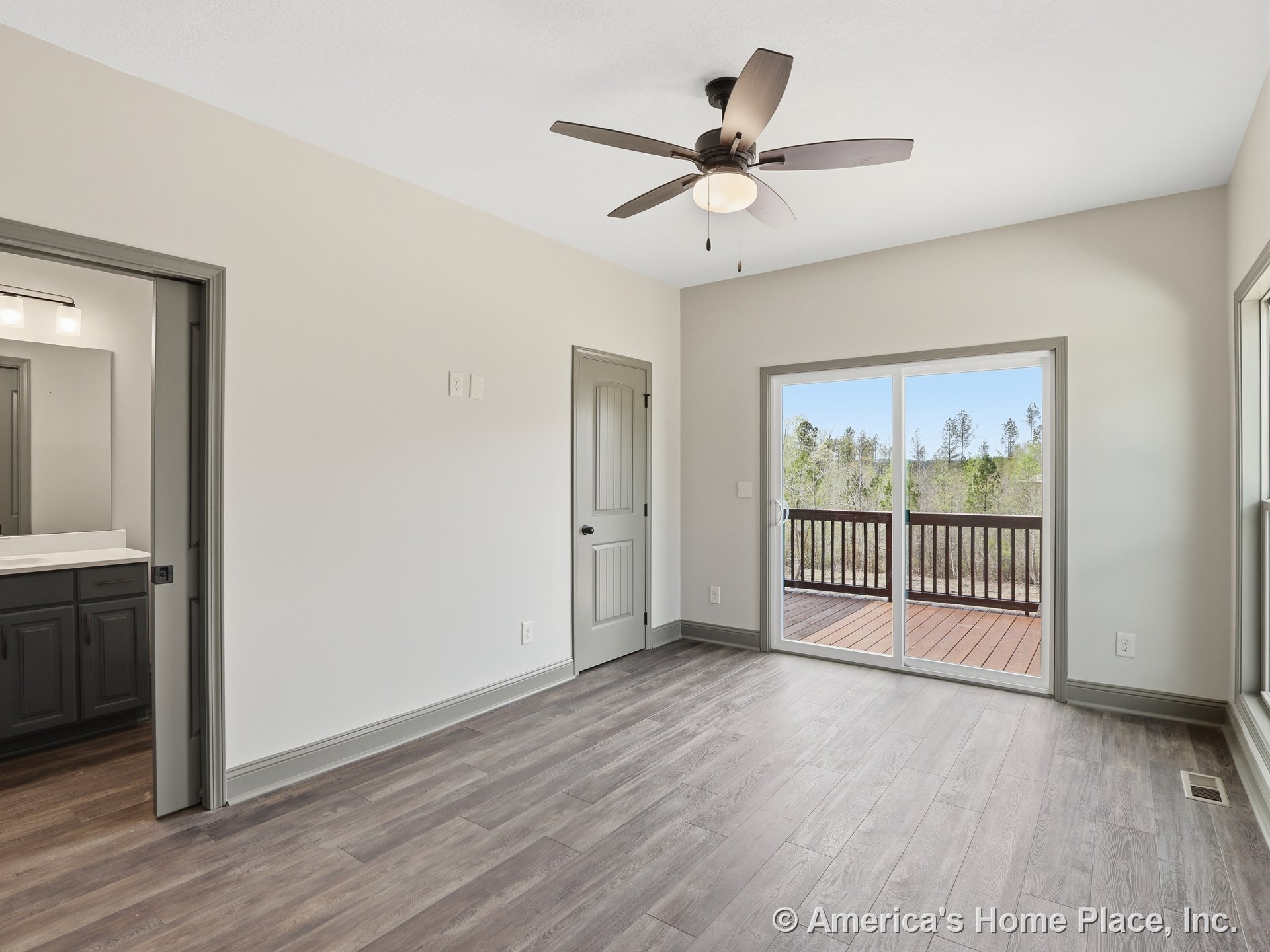 Bedroom with wood-look plank flooring, ceiling fan and integrated light, sliding glass door opening to outdoor deck with railing, gray painted trim and doors, attached bathroom