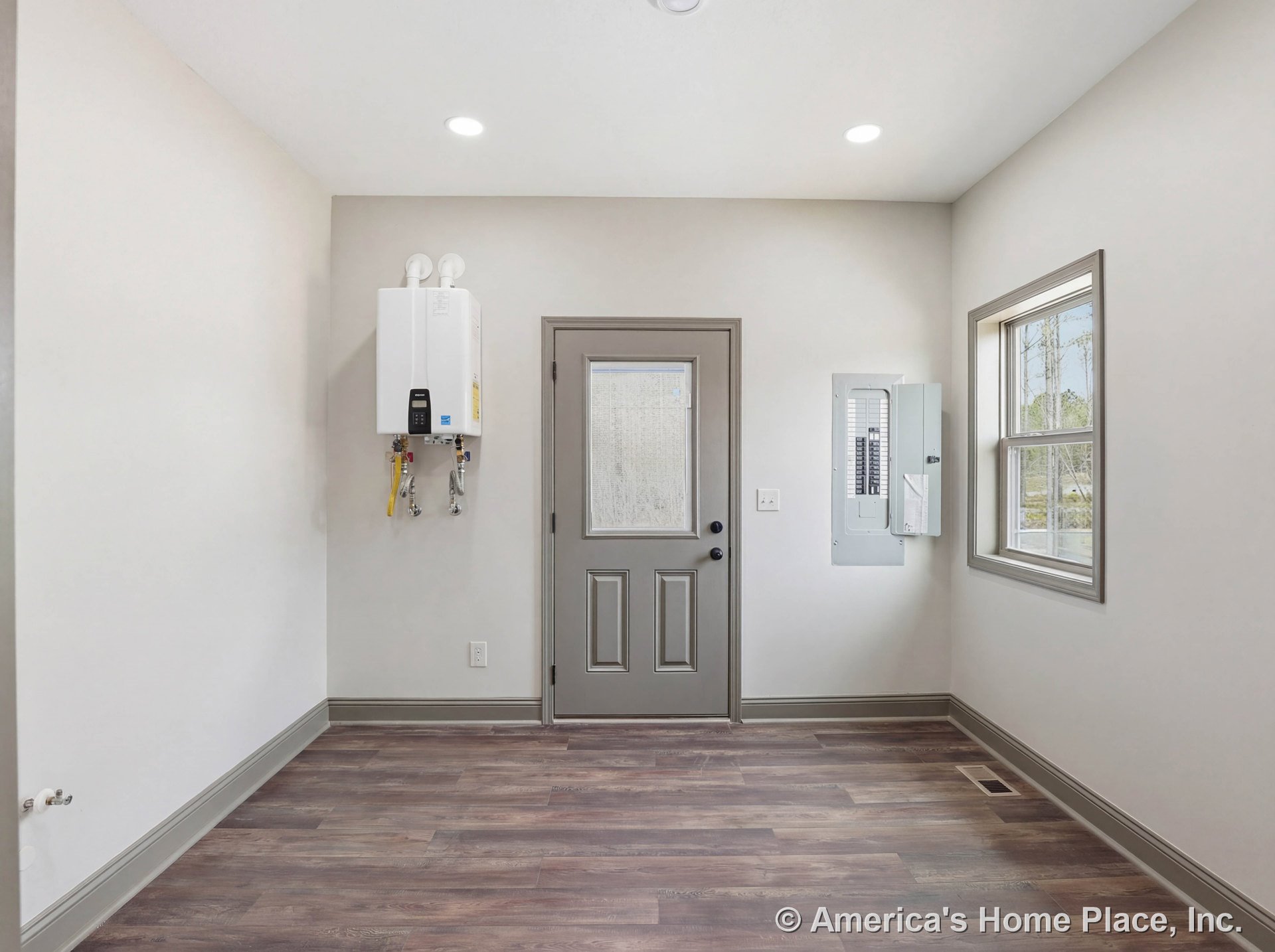 Utility room with tankless water heater and electrical panel, exterior door with double-pane window and gray trim, wood-look vinyl flooring, recessed ceiling lights, neutral walls