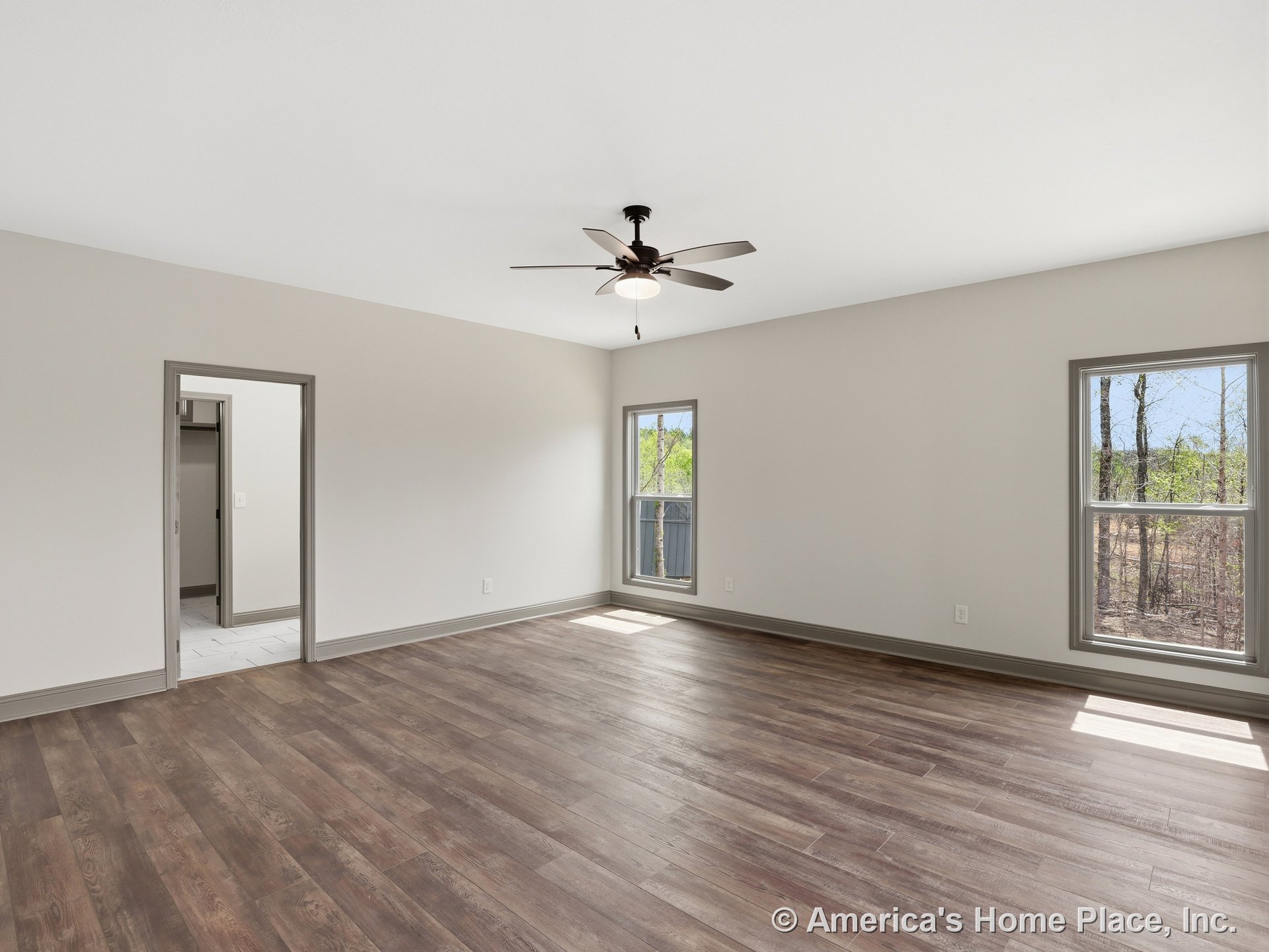 Wood-look plank flooring, neutral painted walls, trimmed windows allowing natural light, ceiling fan with integrated light fixture, baseboard trim, open doorway leading to tiled