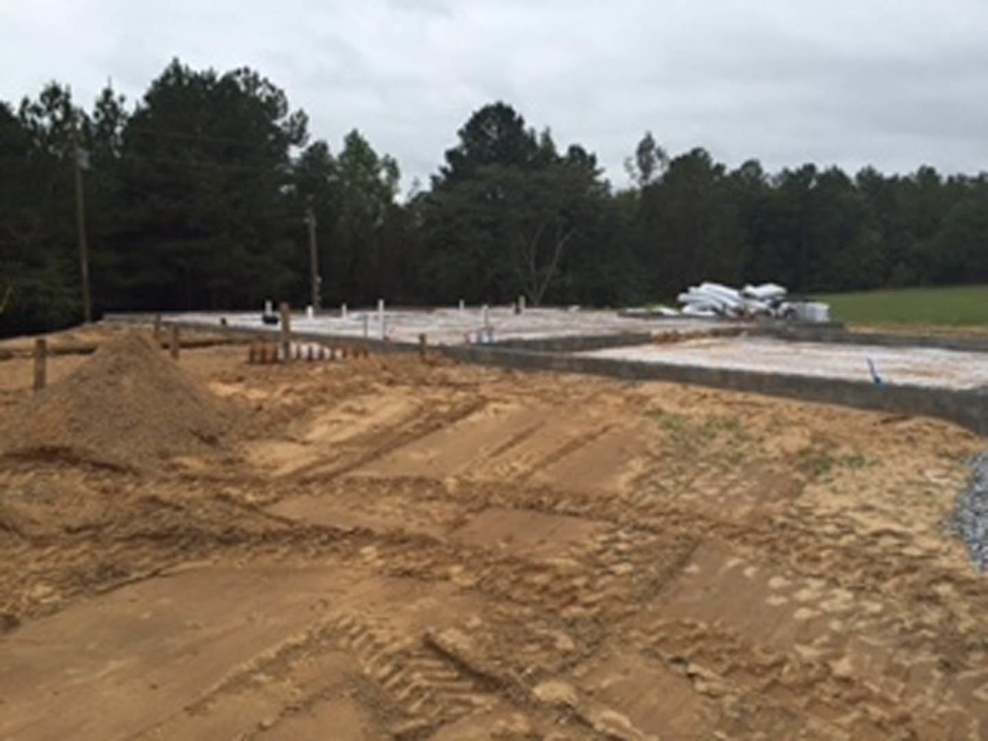 Dirt field with tire tracks bordered by a group of trees under a cloudy sky