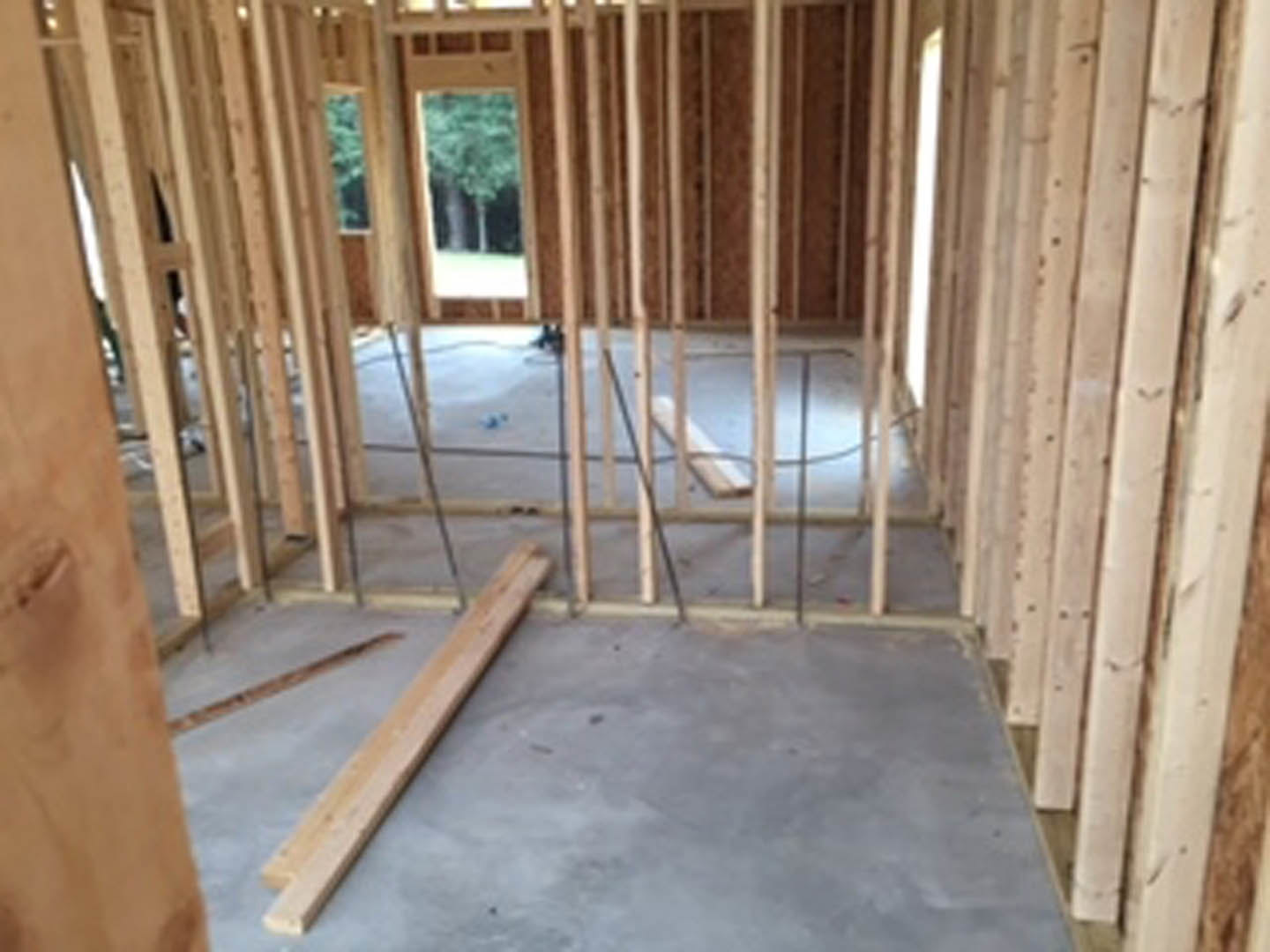Exposed wood ceiling beams above a concrete floor, large window letting in natural light, unfinished wood framing visible