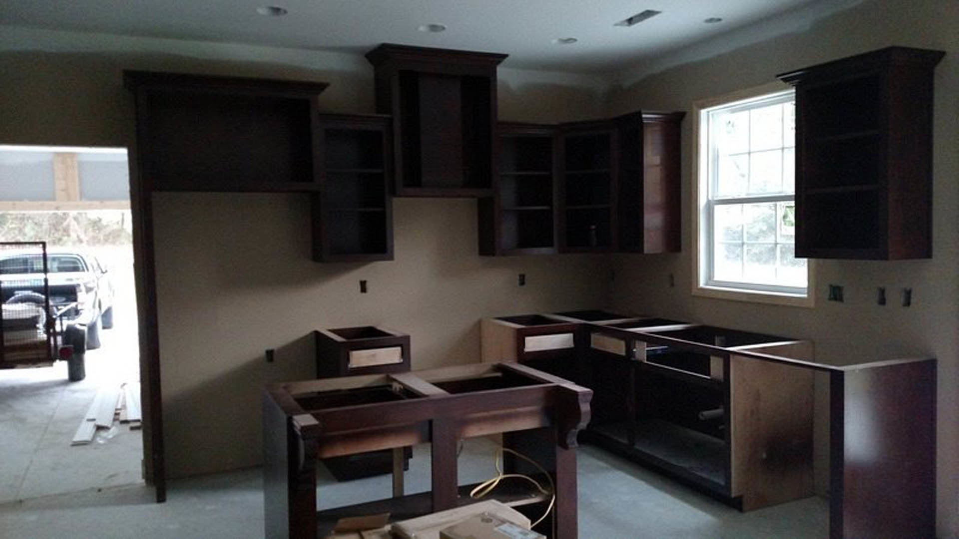 Kitchen with dark wood cabinets, white-framed window, dark wooden shelf, light countertops, and a dining table featuring a central cutout.