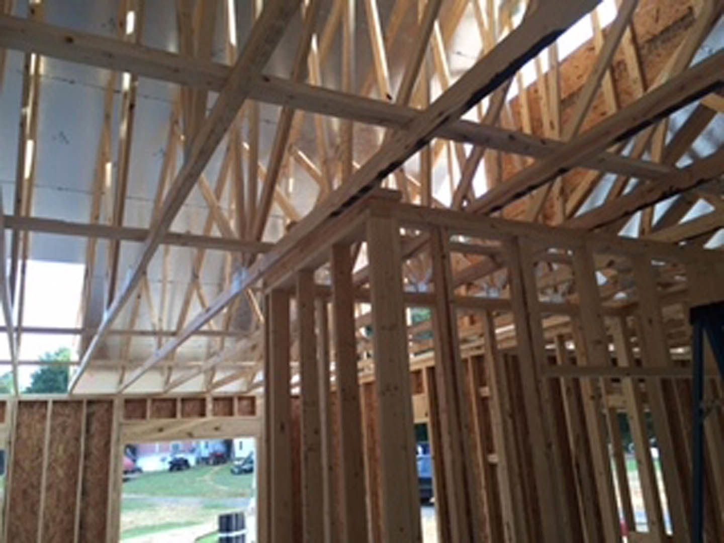 Exposed wood framing with vertical and horizontal beams inside a partially constructed house, natural daylight streaming through open walls and ceiling