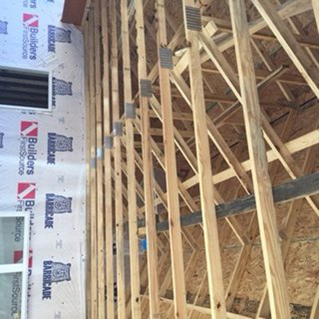 Exposed wood framing of a house under construction with a white sign displaying blue and red logos in the foreground