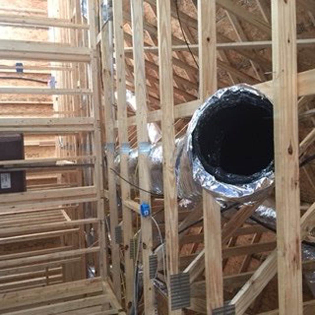 Exposed wood framing with visible pipes and metal ducts, white sign attached to brown wood, black hole in pipe, blurry black electrical box