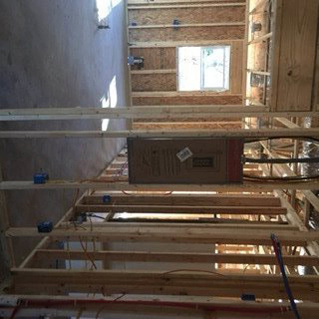 Exposed wood framing and beams inside a house under construction, with a white sticker and rectangular object attached to a brown surface, and a blurry hand visible in the