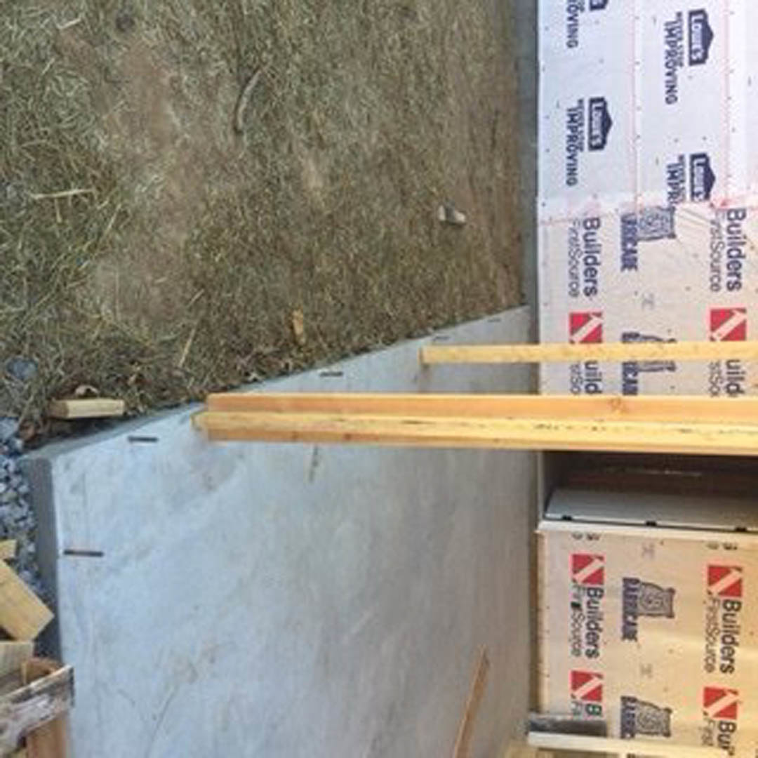 Stacked wooden beams and lumber beside a concrete wall, with a white box displaying black and red logos in the foreground.