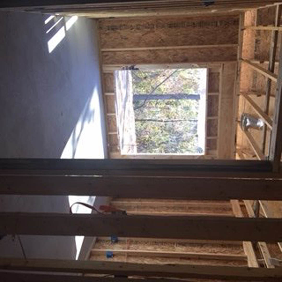 Sunlit room featuring a large window overlooking a leafy tree, wood plank ceiling with exposed wiring, and smooth painted walls.