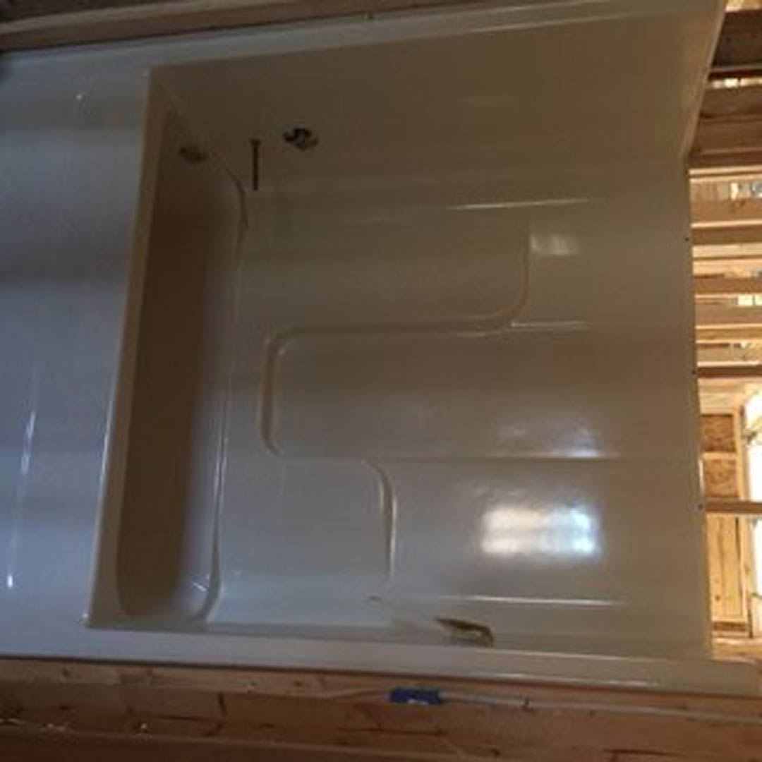Freestanding white bathtub near a window in a modern bathroom with light walls and wood flooring