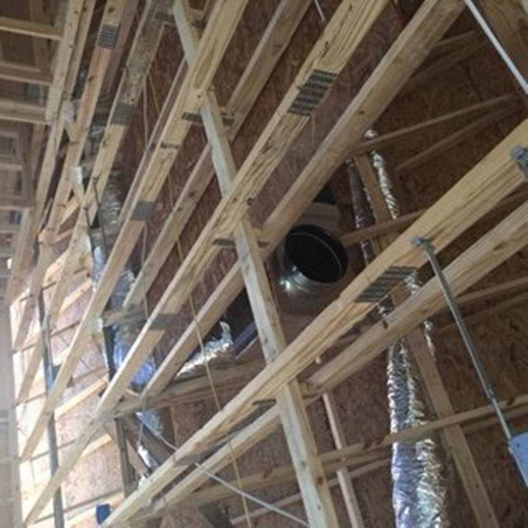 Exposed wood framing and beams with visible insulation inside a partially constructed residential interior