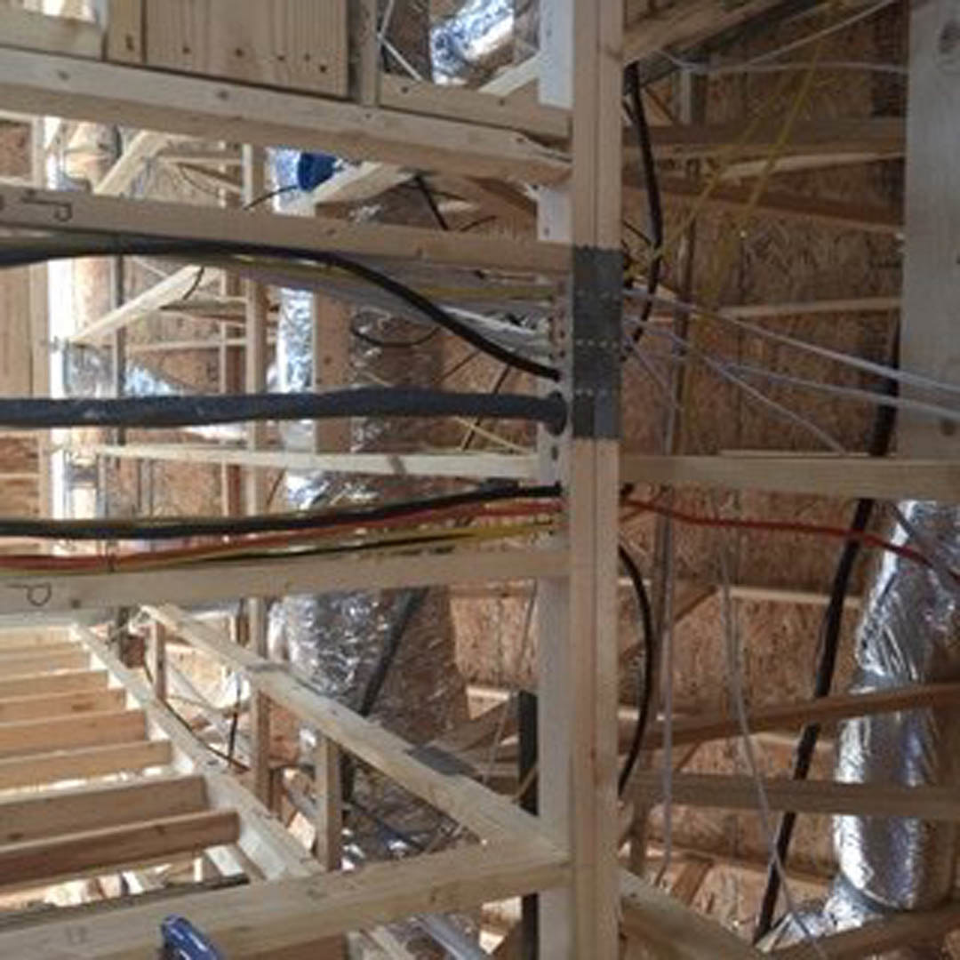 Exposed wood framing with visible electrical wires and cables running through beams inside unfinished residential construction