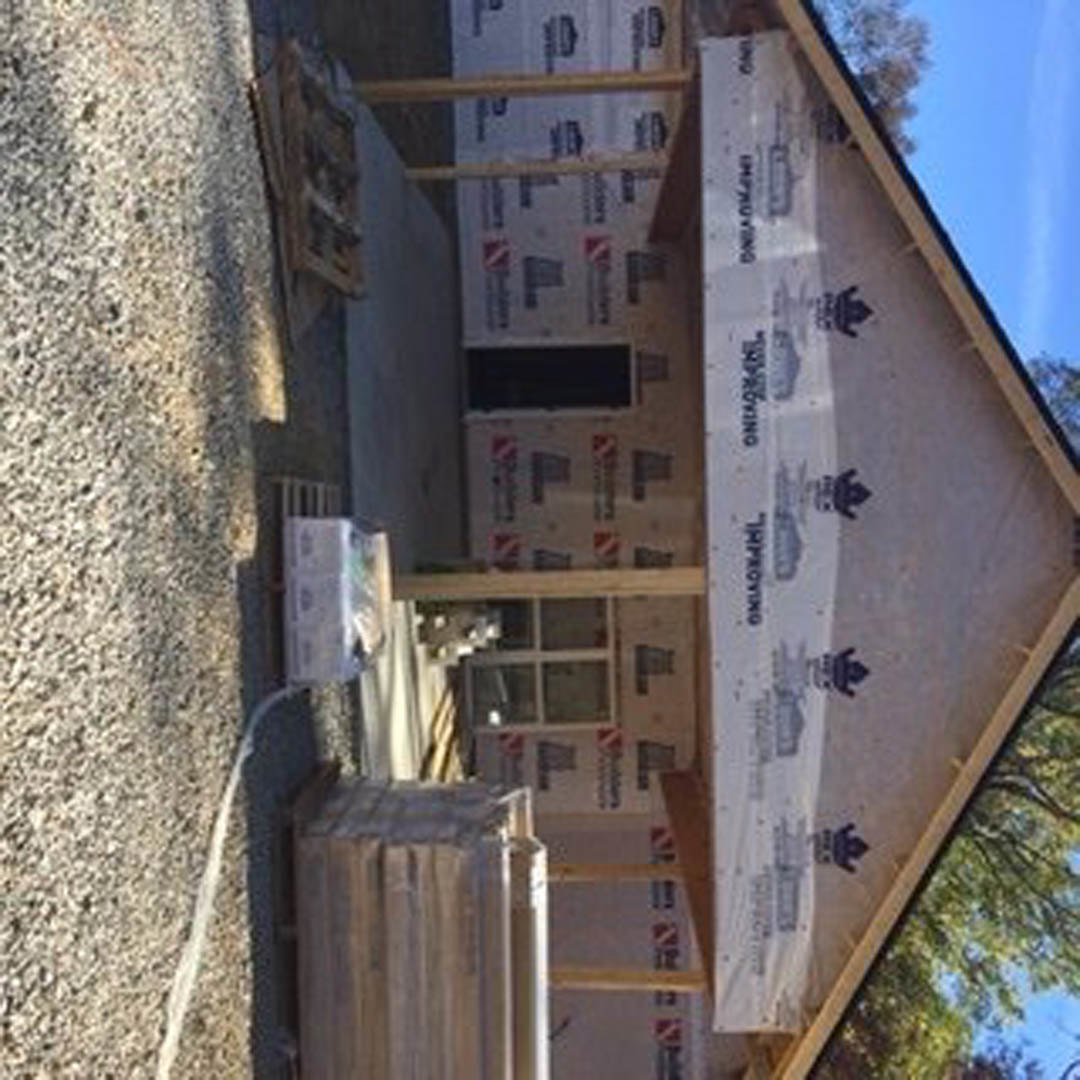 Framed house under construction with exposed wood beams, insulation panels, plastic sheeting, and unfinished window openings