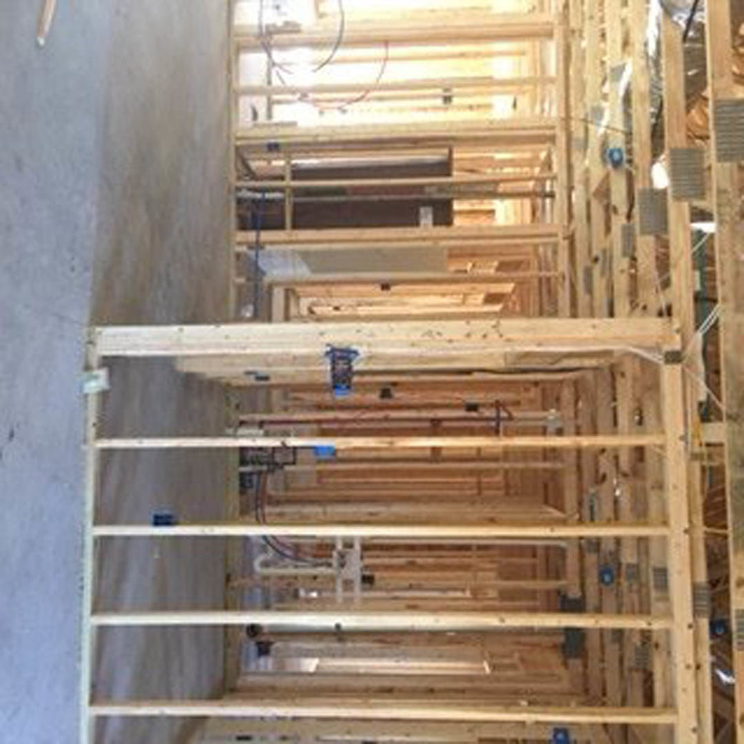 Exposed wooden framing and lumber planks forming the structure of a house under construction, with a blurred leg partially visible in the foreground