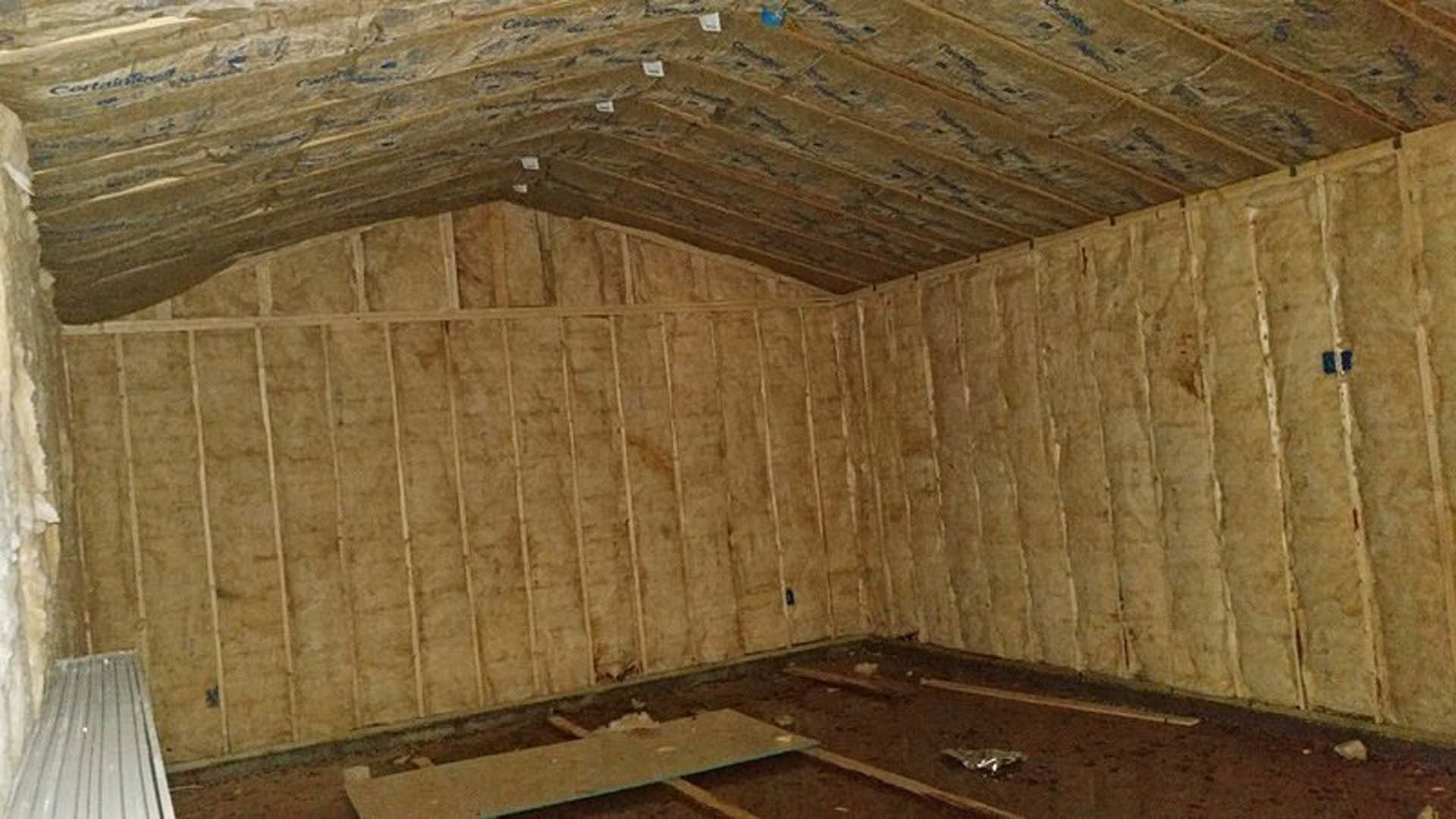 Wood-paneled walls and ceiling with exposed wooden beam, plywood boards, metal plate and aluminum foil on unfinished floor