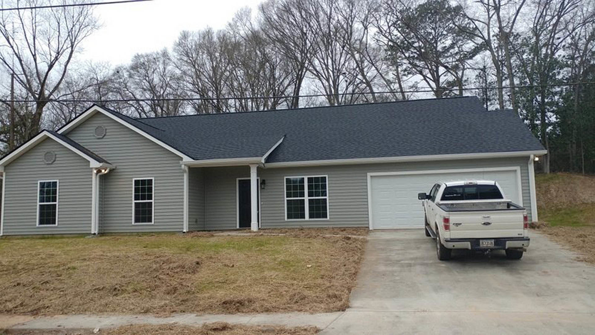 White pickup truck parked on driveway in front of modern house with black door, multi-pane windows, manicured grass lawn, and tree in yard