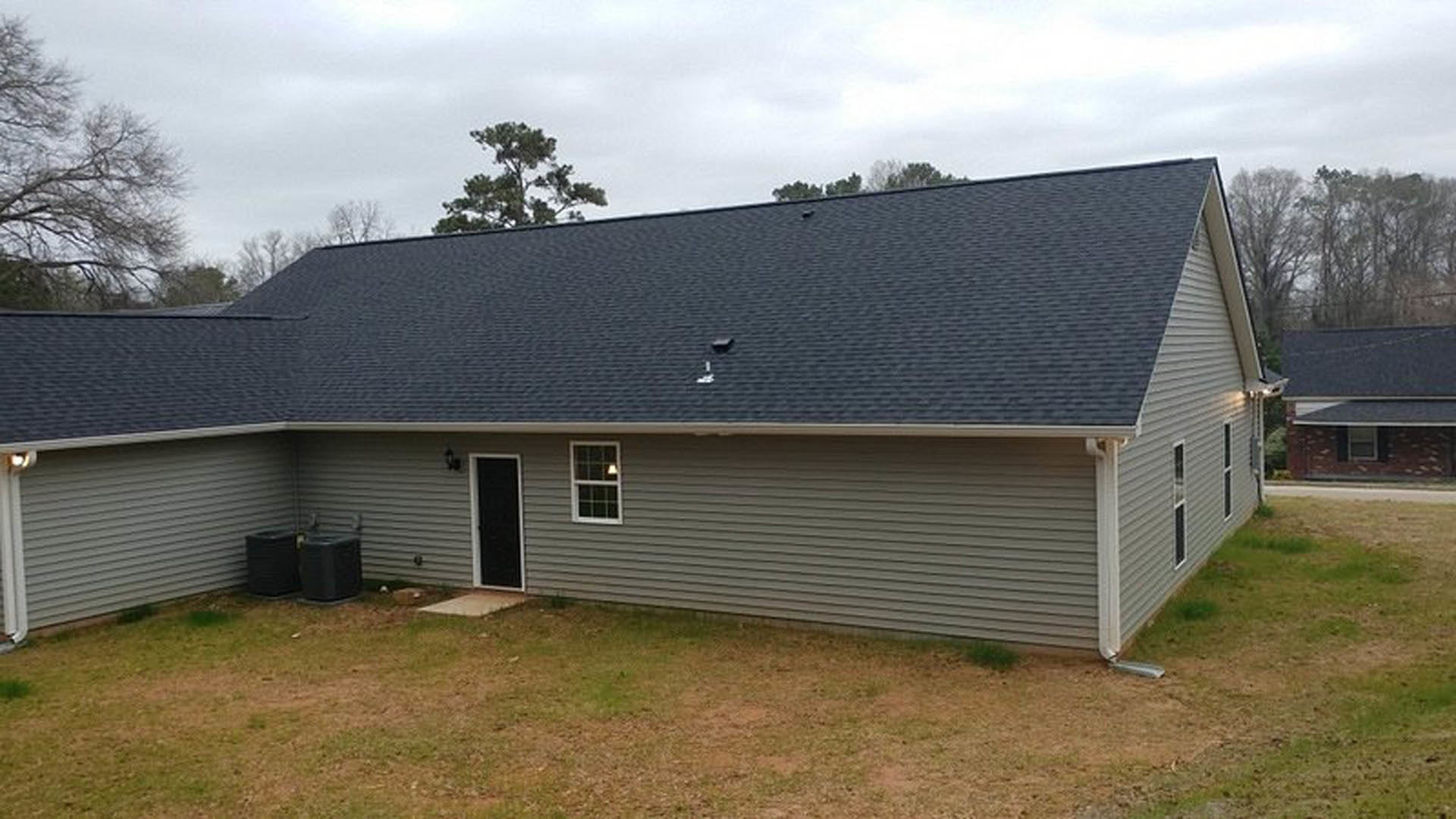 Two-story house with black roof, white siding, black front door with white trim, illuminated window, manicured green lawn, black bins beside exterior wall, cloudy sky overhead