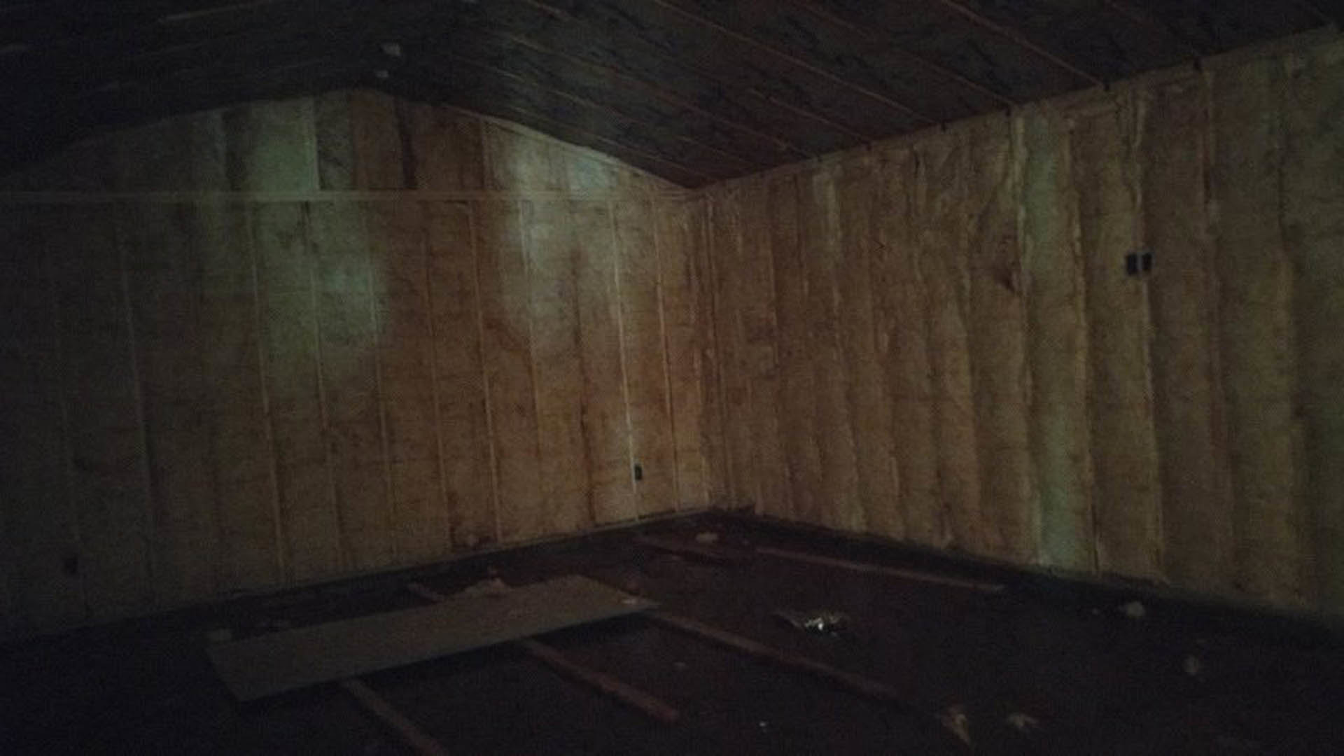 Wood paneled wall and wooden ceiling in a dimly lit room with metal flooring, partially visible window and blurred figure