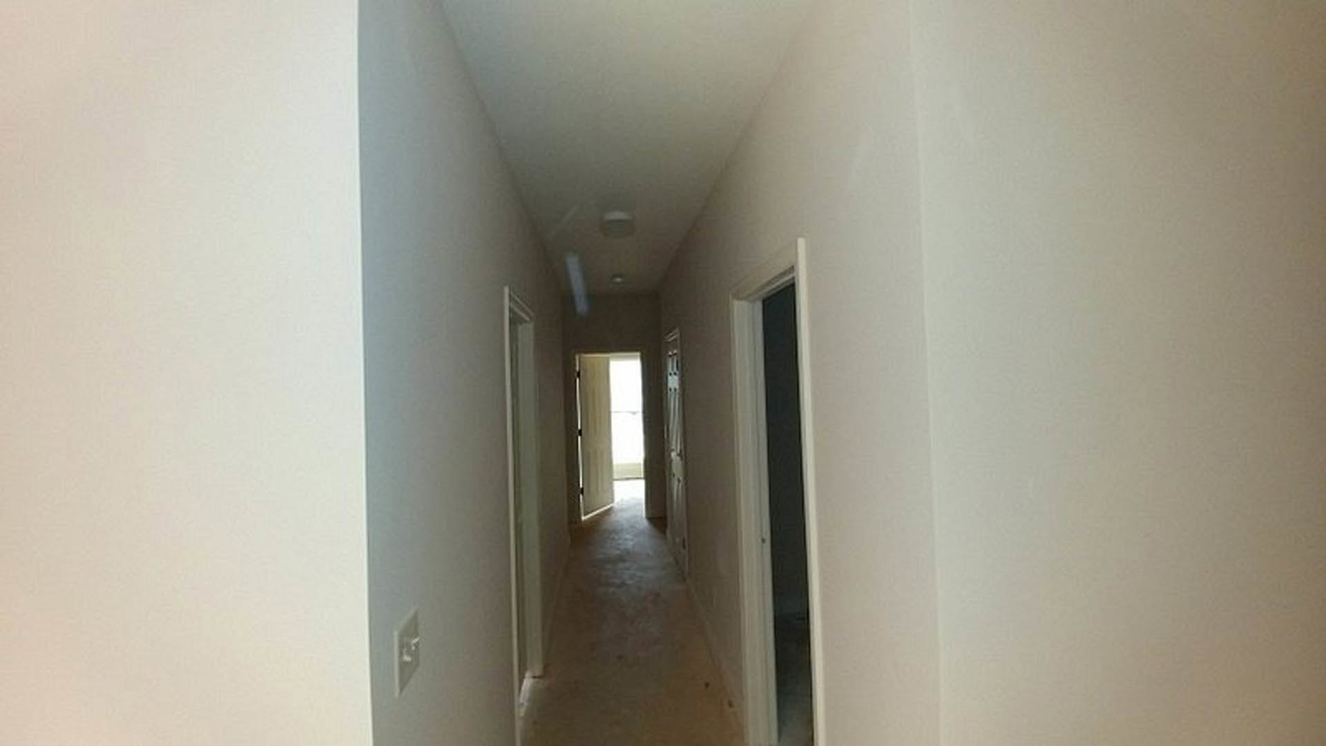 Hallway with smooth white plaster walls, black trim border, light switch, and neutral flooring