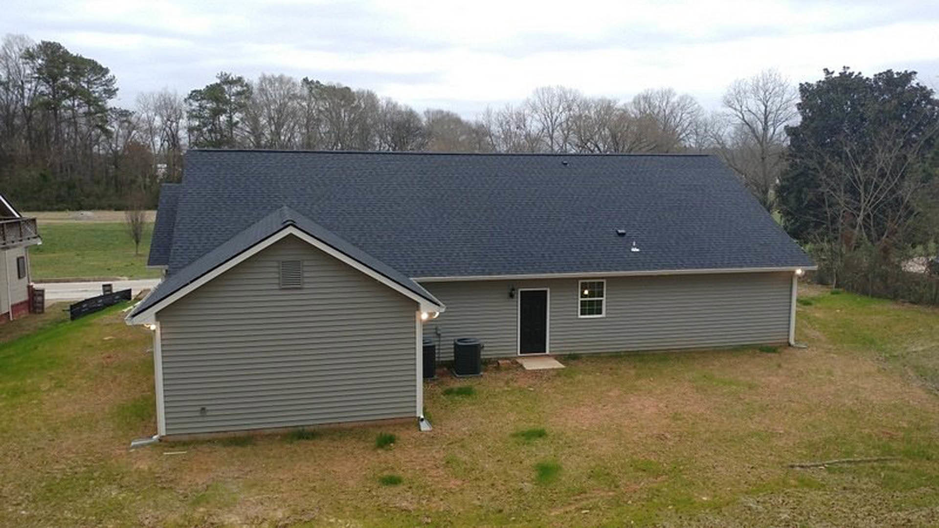 White siding house with black front door, rectangular vent, manicured green lawn, mature trees in background, gabled roof, clear sky