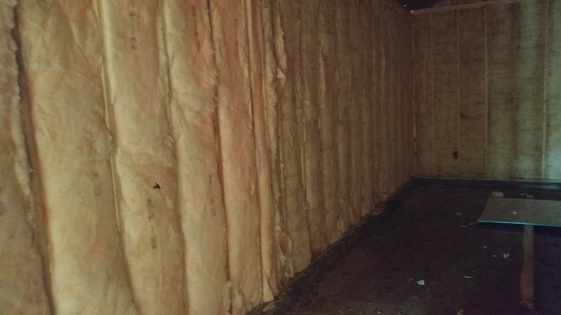 Exposed wall filled with thick insulation panels in a dimly lit room with dark flooring and wooden planks visible.