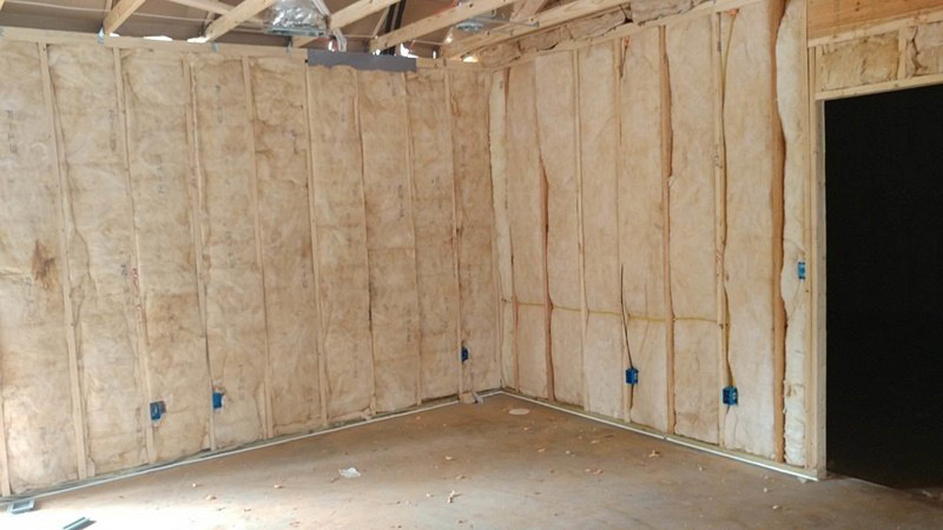 Room featuring wood plank walls and ceiling, concrete floor with white border, wall section showing insulation, black board with white border, and a blurred person’s head in