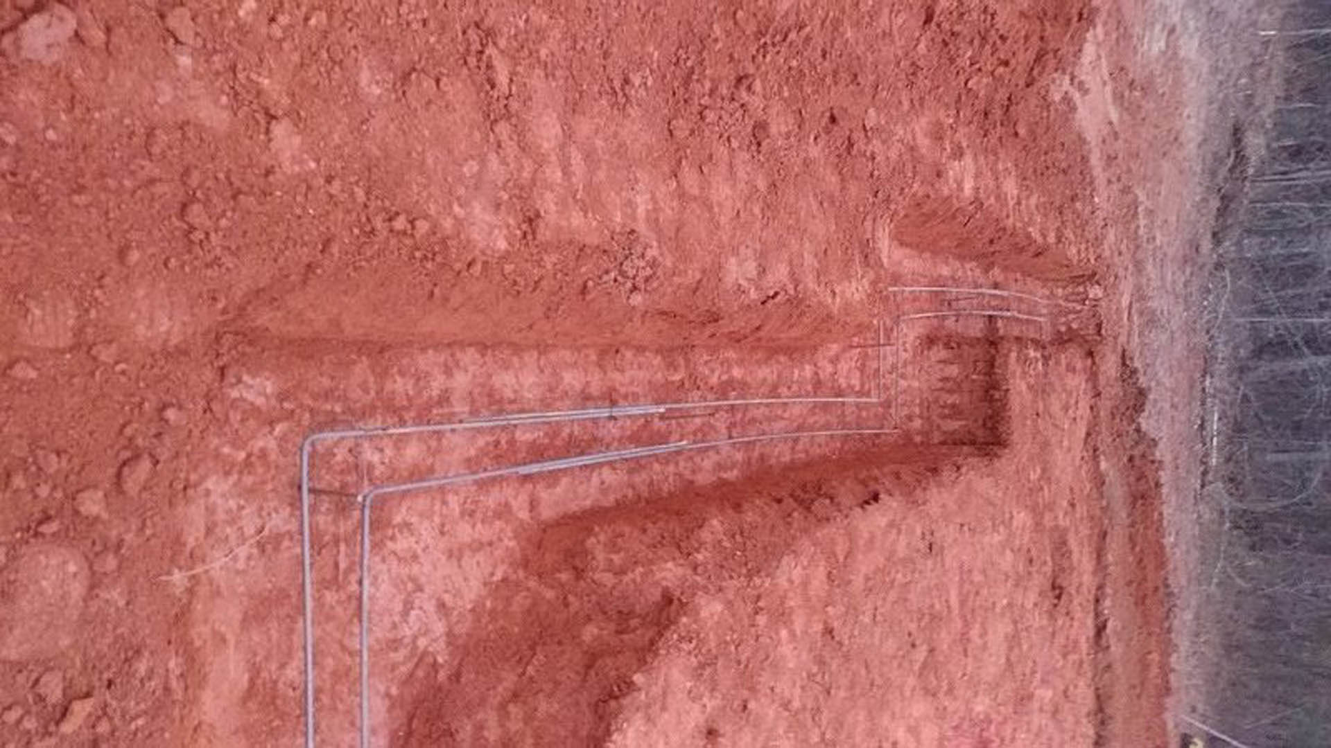 Exposed wire partially buried in brown dirt with small rocks and rough ground texture