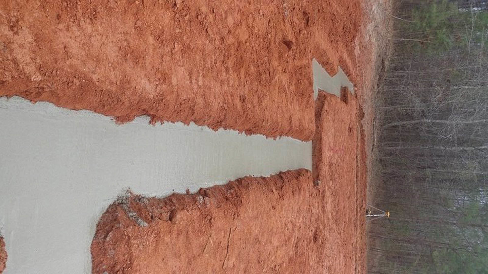 Excavated dirt with a deep hole and wooden stake marking foundation area