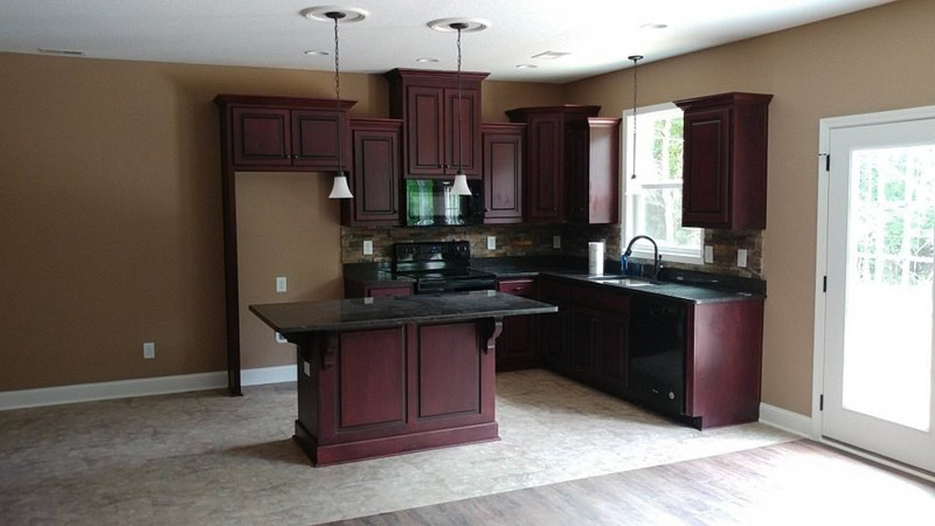 Kitchen with dark wood cabinets, black countertop, stainless steel sink, and light-colored flooring