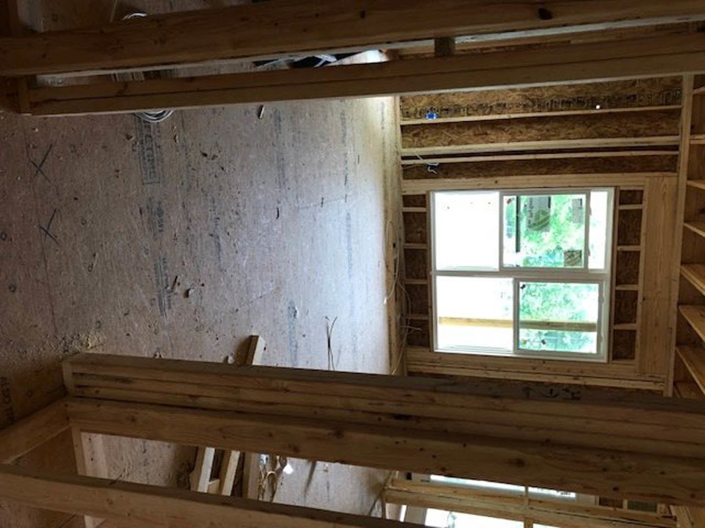 Exposed wood framing and beams with unfinished walls, large window providing daylight, construction materials visible throughout room