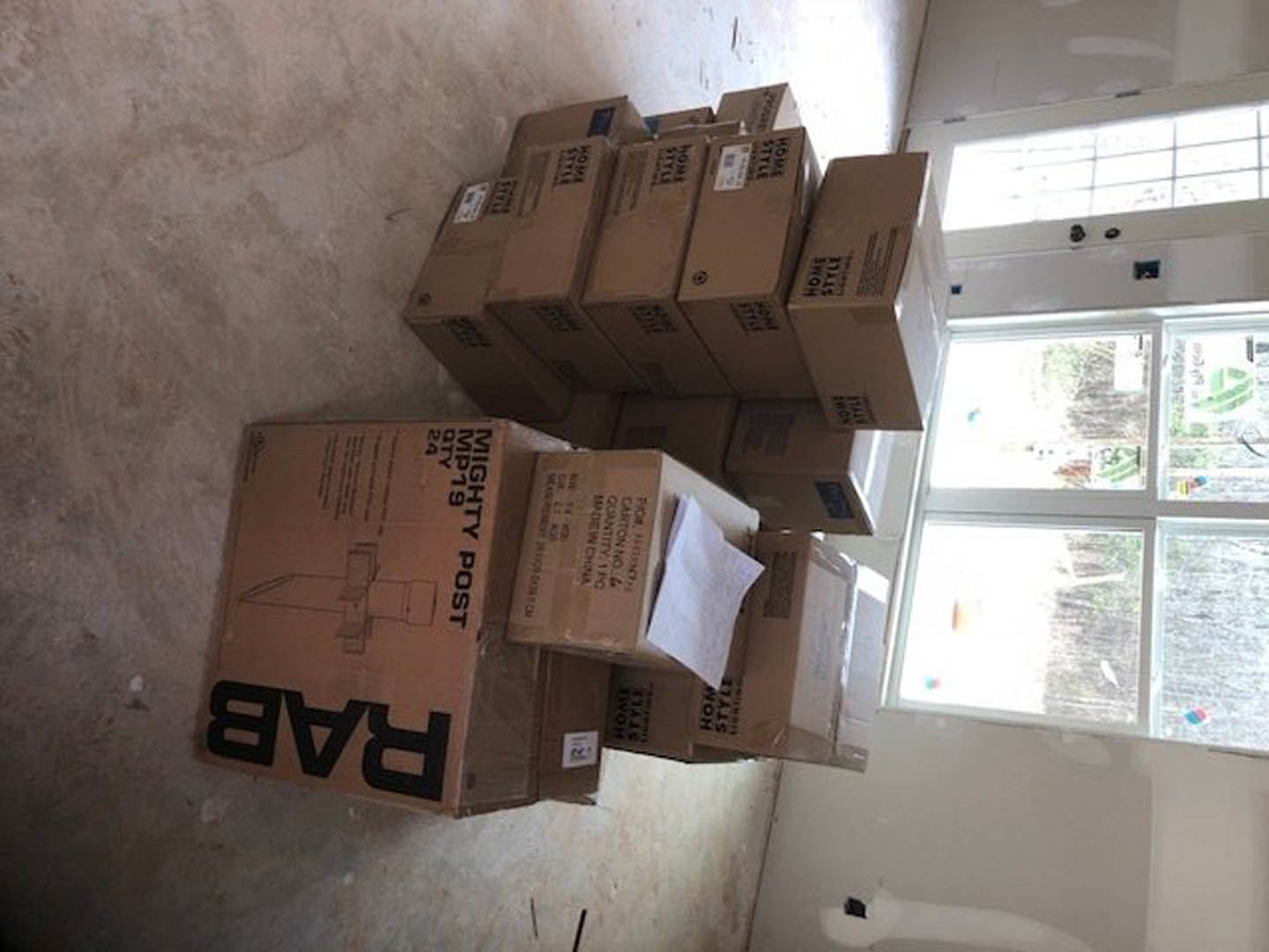 Stacked cardboard moving boxes on light hardwood floor beside white walls and large window with outdoor view