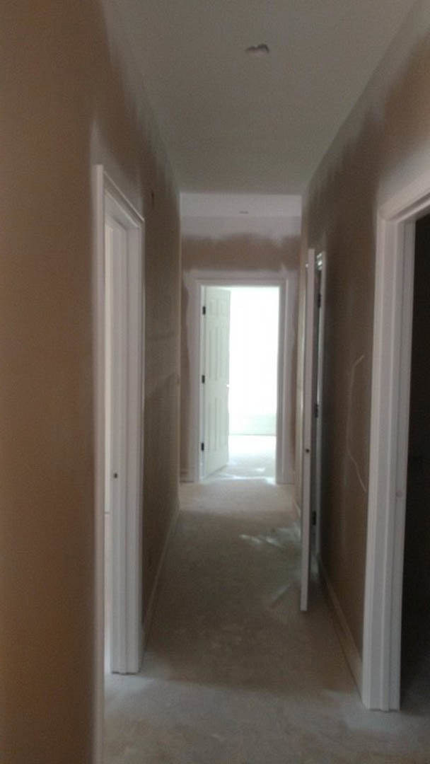 Hallway with smooth white plaster walls, matching white doors, light wood flooring, and simple crown molding