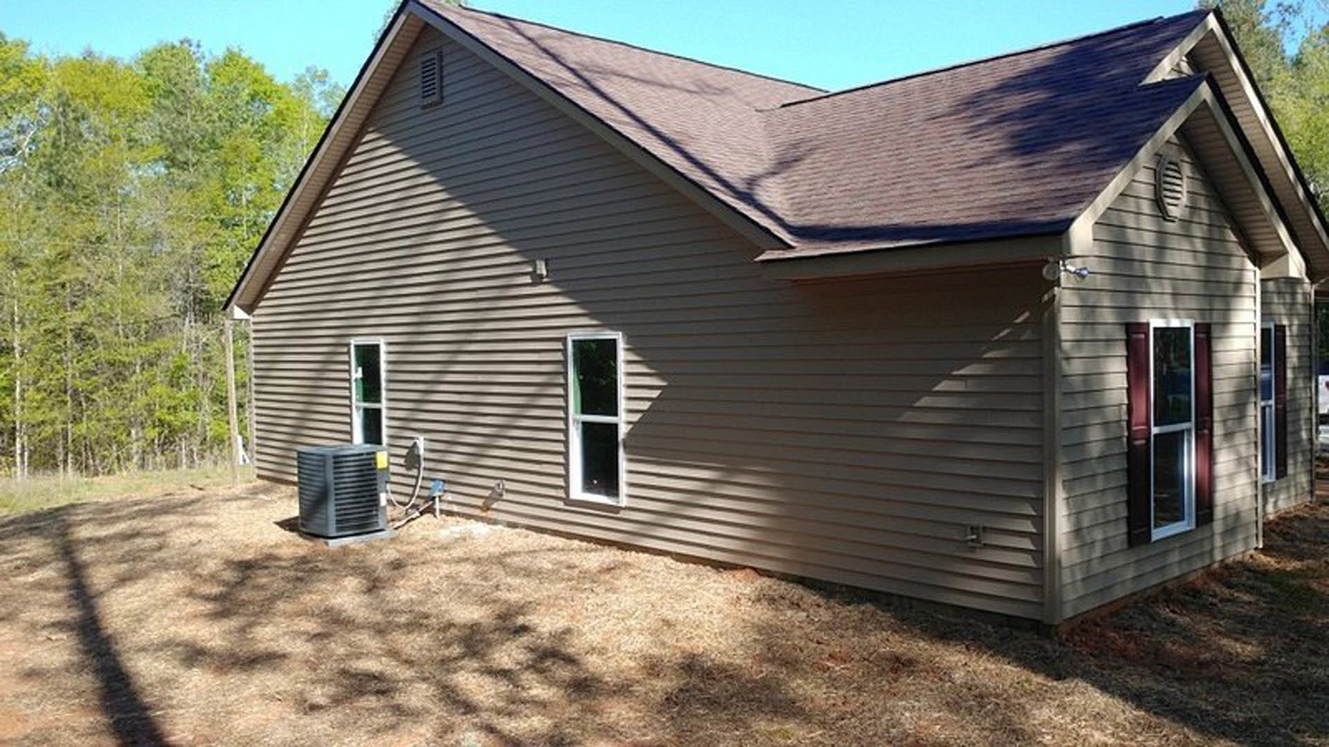 Modern cottage-style home with gray siding, white-framed windows, black outdoor heater on rear patio, pitched roof, and mature trees in background