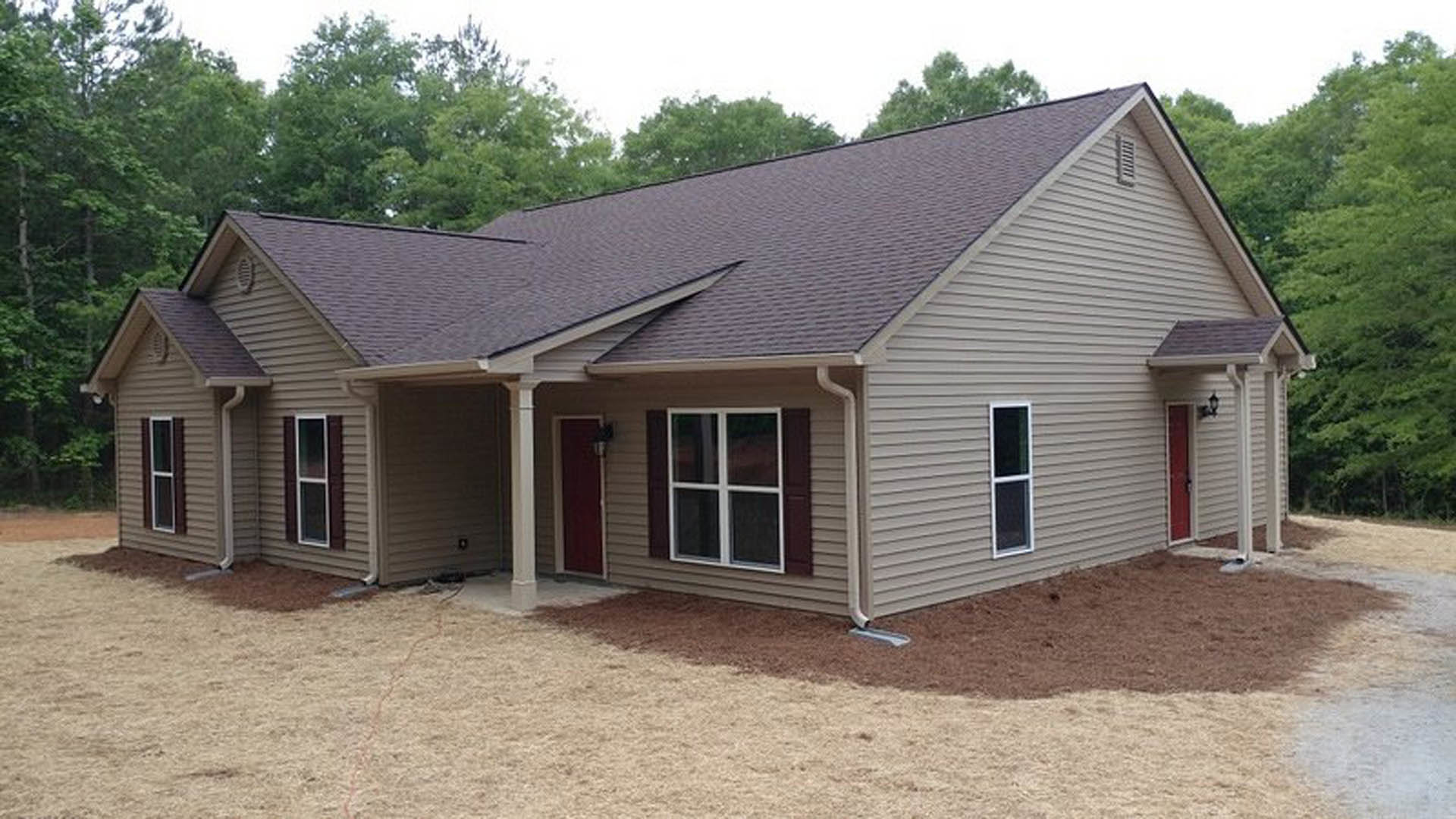 Two-story home with white-framed windows, red front door, covered porch, and expansive paved driveway surrounded by mature trees