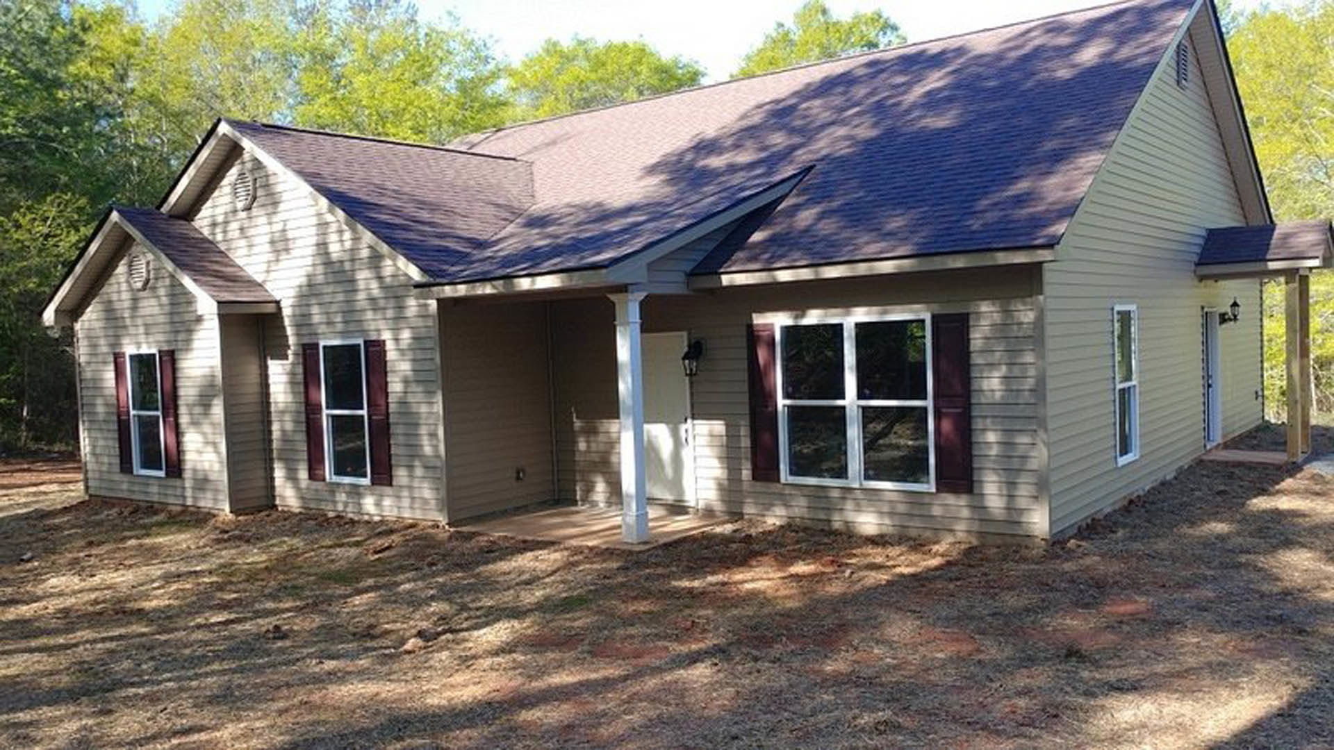 Two-story house with covered front porch, white door, and windows featuring white and red frames; surrounded by trees and greenery under a blue sky.