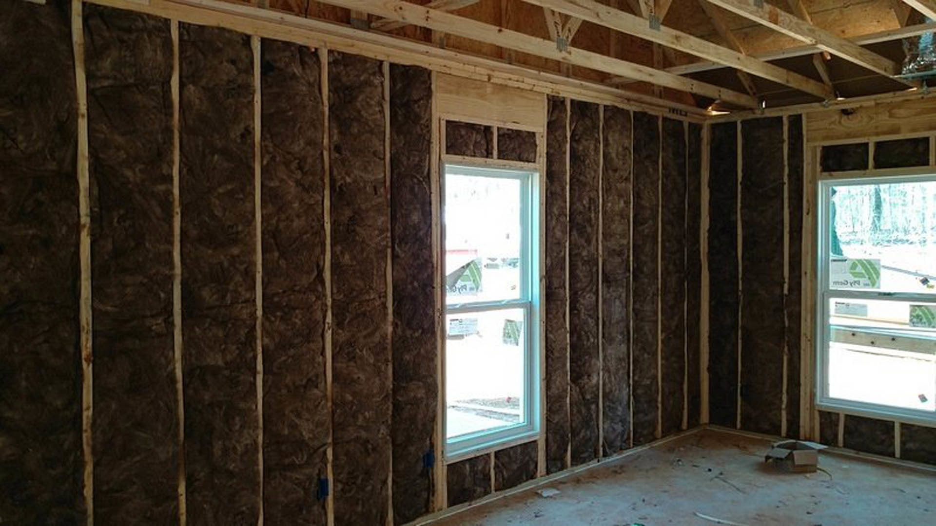 Room with two windows, wooden plank accent wall, light wood flooring, and ceiling beams; papers and a sign attached to one window.