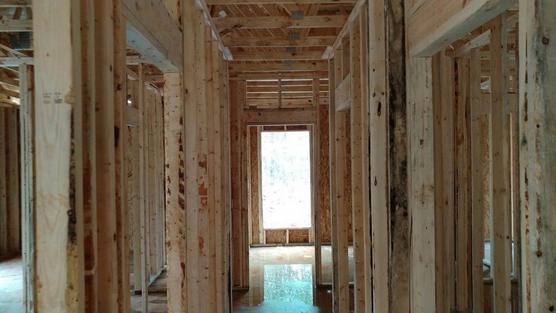 Living room with exposed wood ceiling beams, large window letting in natural light, white walls, and hardwood flooring