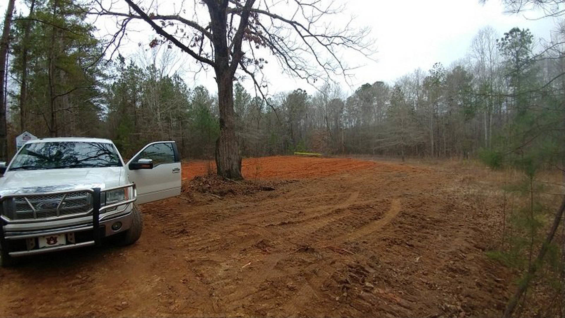 White truck parked on a dirt lot with visible tire tracks, surrounded by trees and open sky